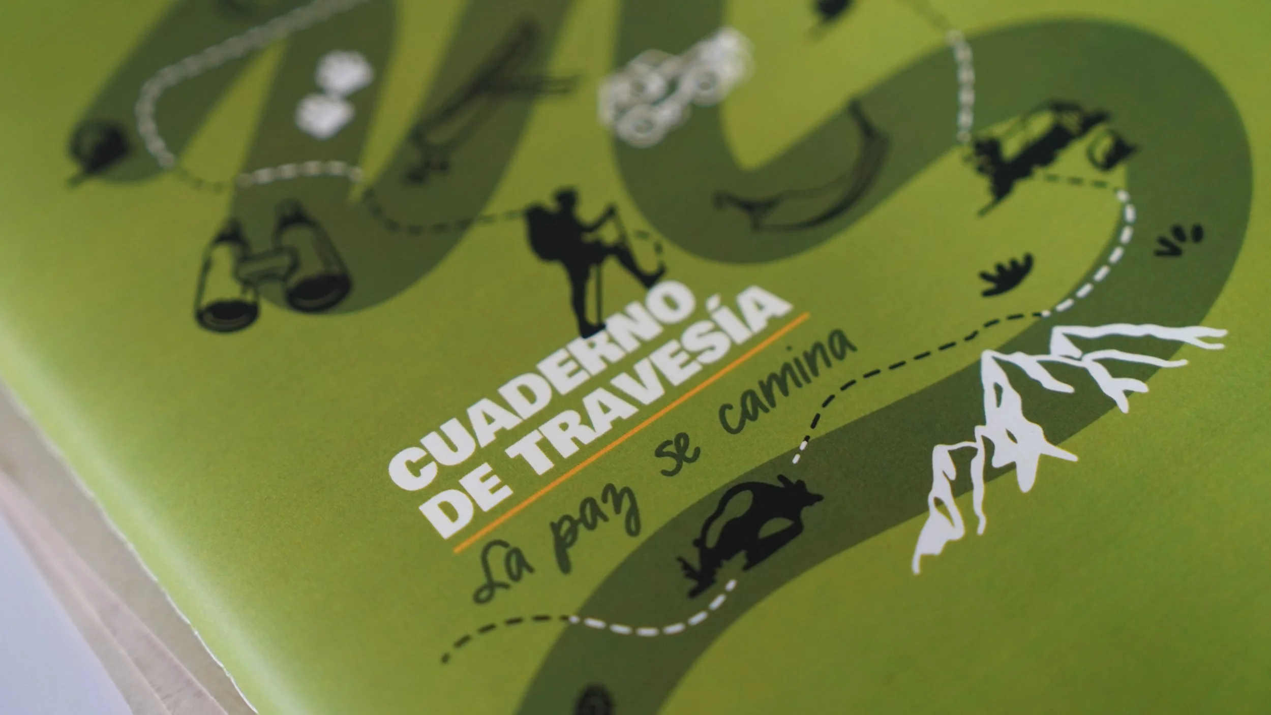 Paquete verde de semillas para caminatas en la naturaleza con ilustraciones de animales, plantas y senderos, con texto en español que dice "Cuaderno de tradiciones de trekking".