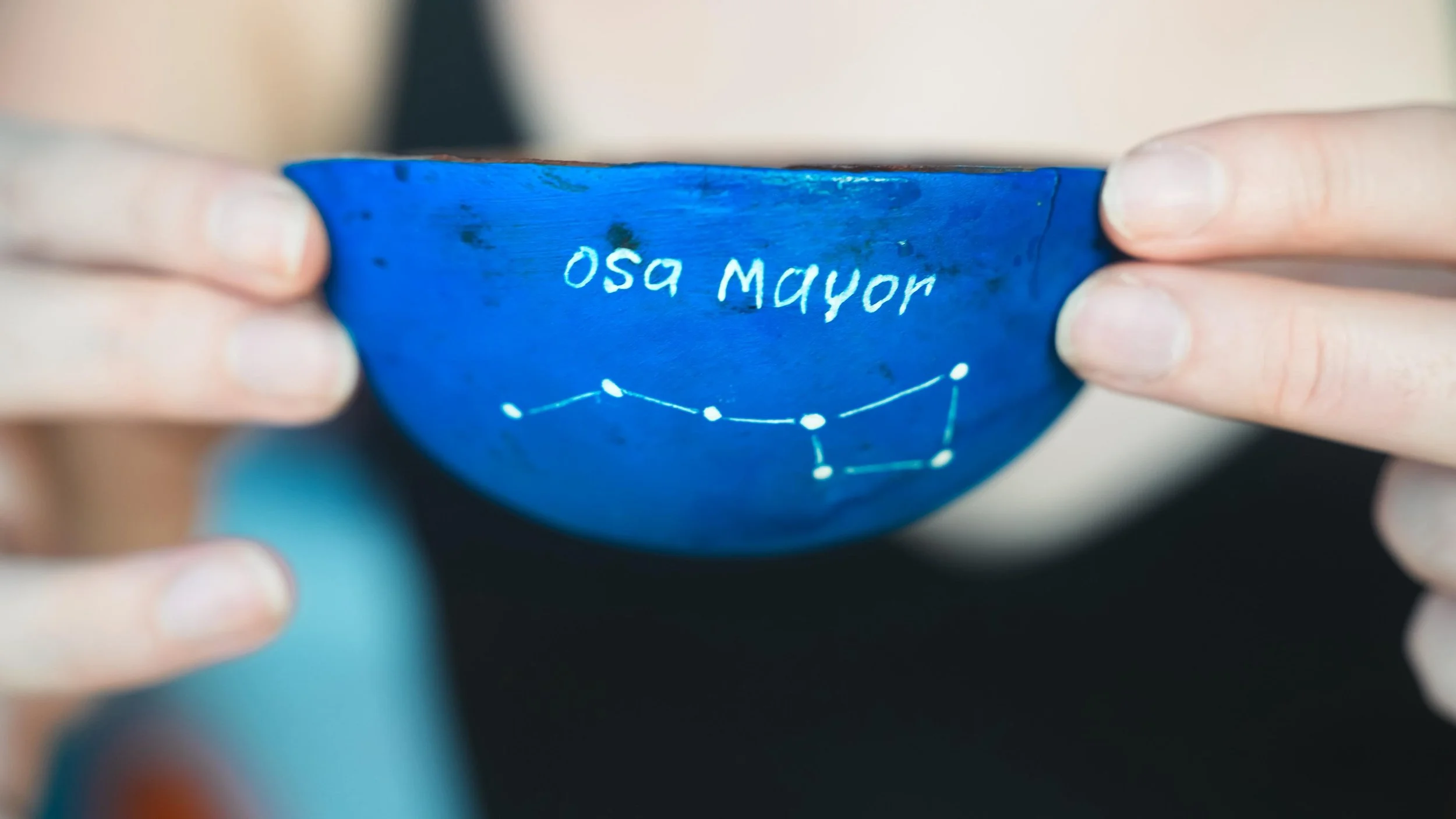 Puente de estrellas con el nombre 'Osa Mayor' en una taza de color azul, sostenida por dos manos.