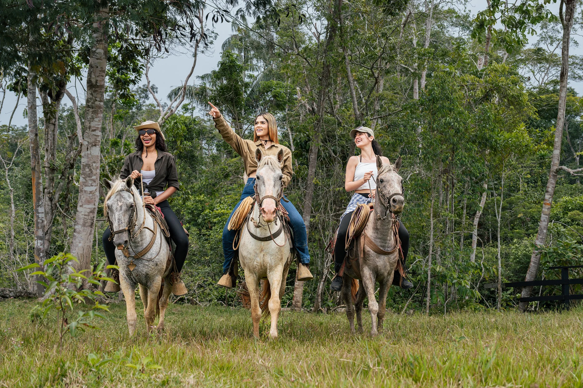 Tres mujeres montando caballos en un bosque de los llanos orientales de Colombia, una de ellas señalando algo en el cielo, sonrientes y disfrutando del paseo.