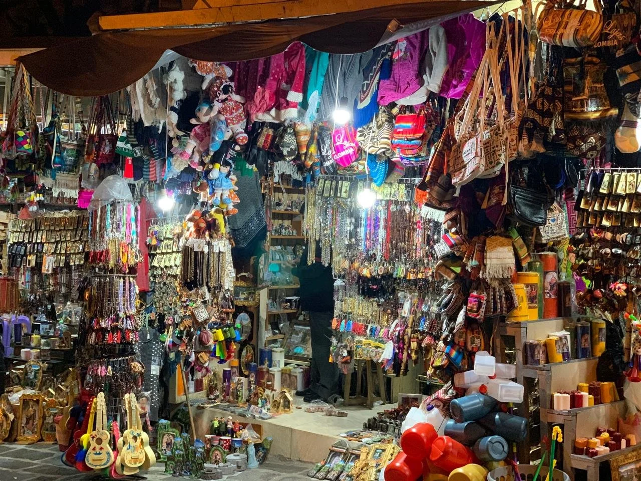 Mezcla de mercancía en un puesto de venta, con muchos accesorios, bisutería, juguetes, bolsas, ropa y decoraciones colgadas y amontonadas en una mesa y en las paredes.