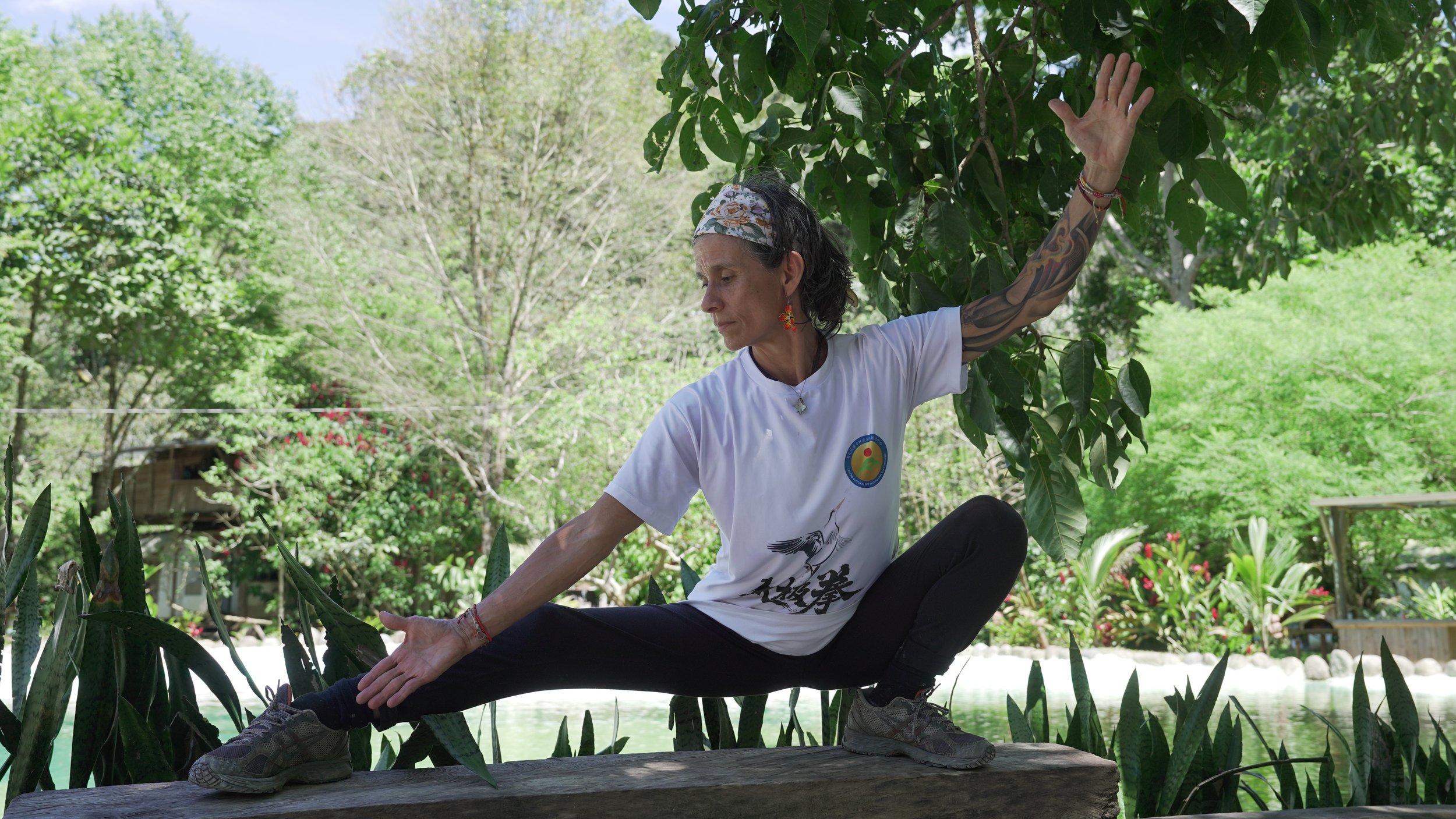Mujer practicando yoga en un entorno natural rodeada de árboles y plantas.