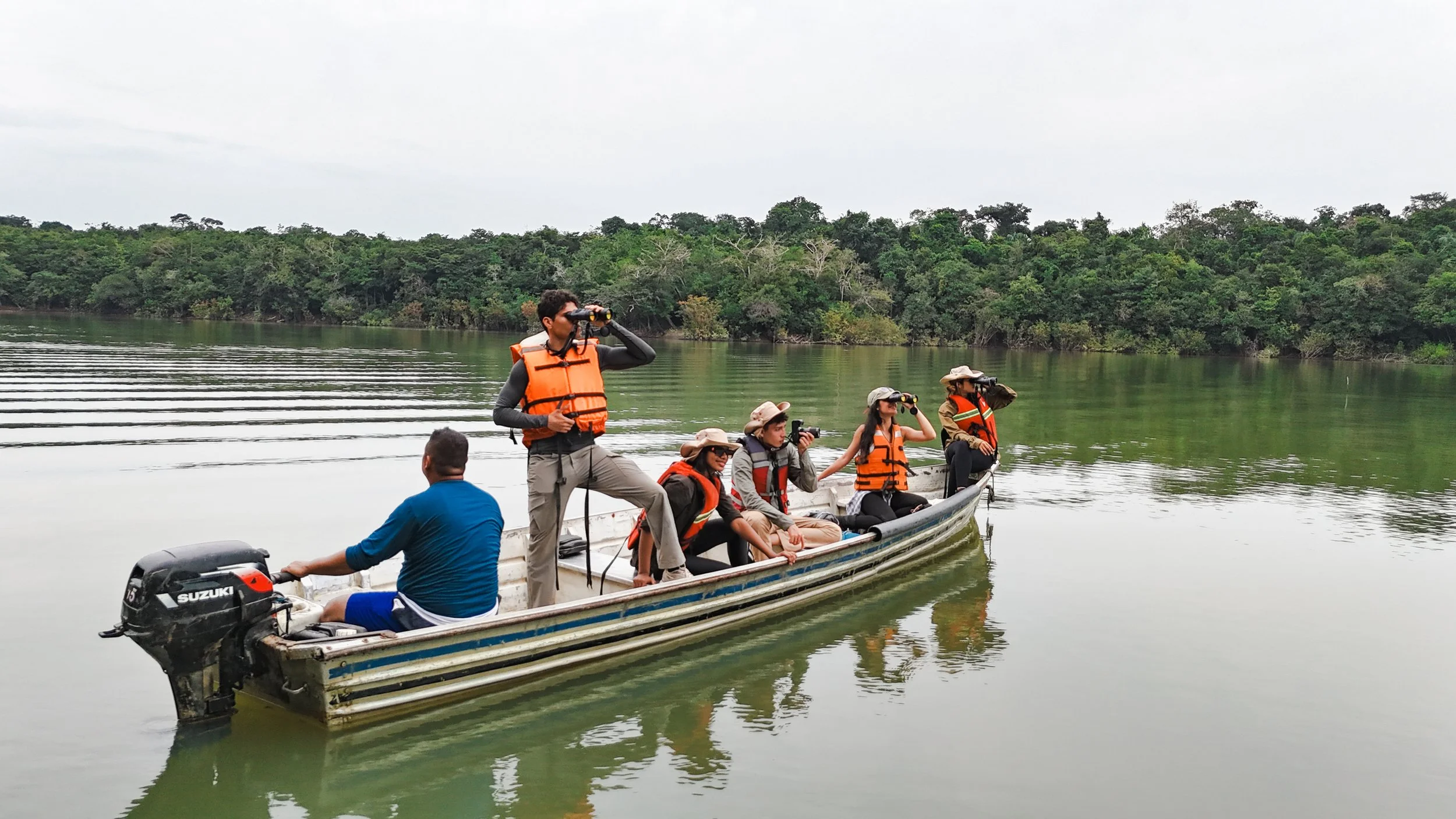 Grupo de turistas con chalecos salvavidas en un bote en río rodeado de árboles