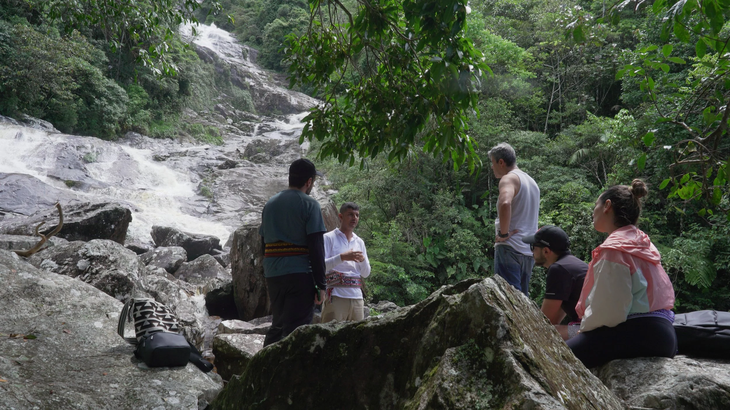 Grupo de personas conversando al borde de una cascada en una selva tropical