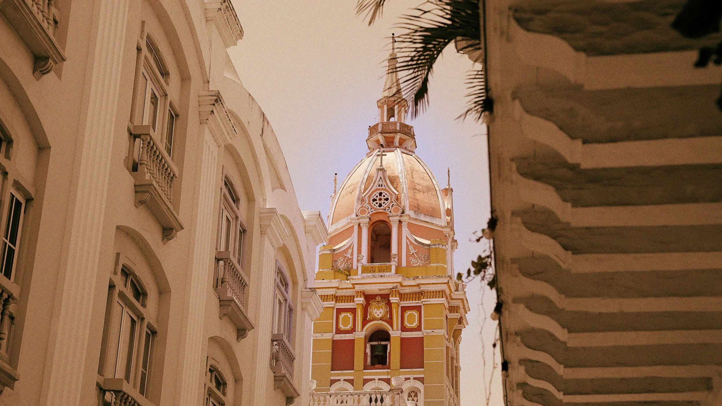 Vista de una torre de iglesia con cúpula decorada en tonos pastel, entre edificios coloniales con balcones.
