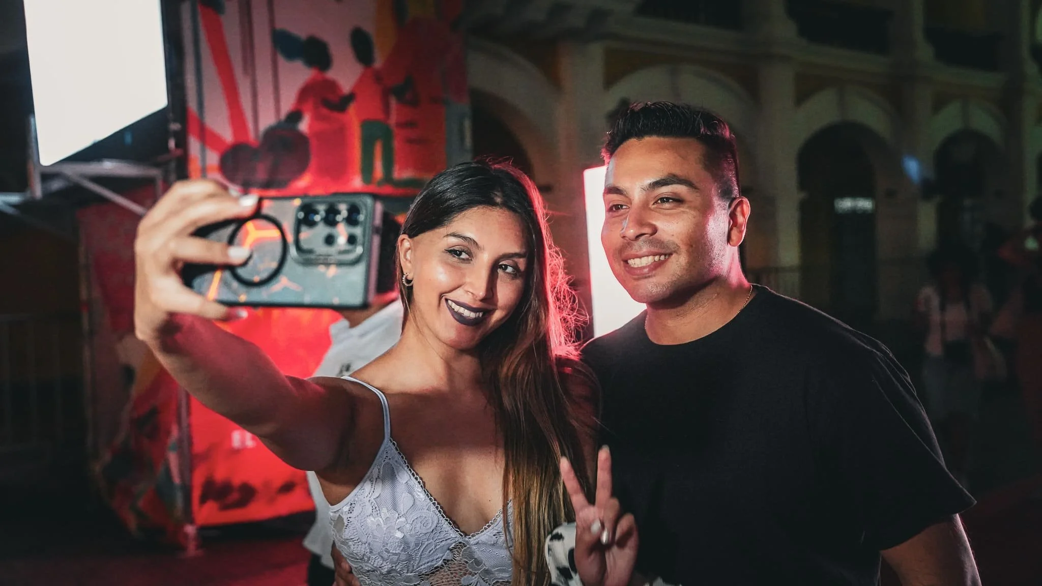 Una pareja tomando una selfie en un lugar con ambiente oscuro y decoraciones con colores vibrantes.