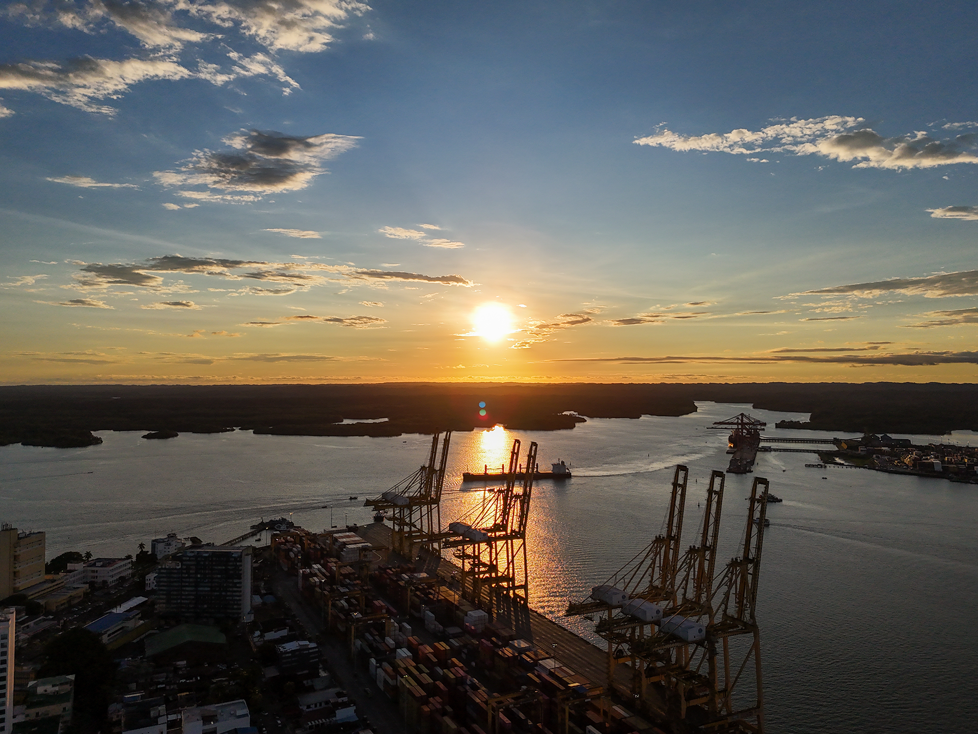 Amanecer en un puerto industrial con grúas y contenedores, río y cielo con nubes.