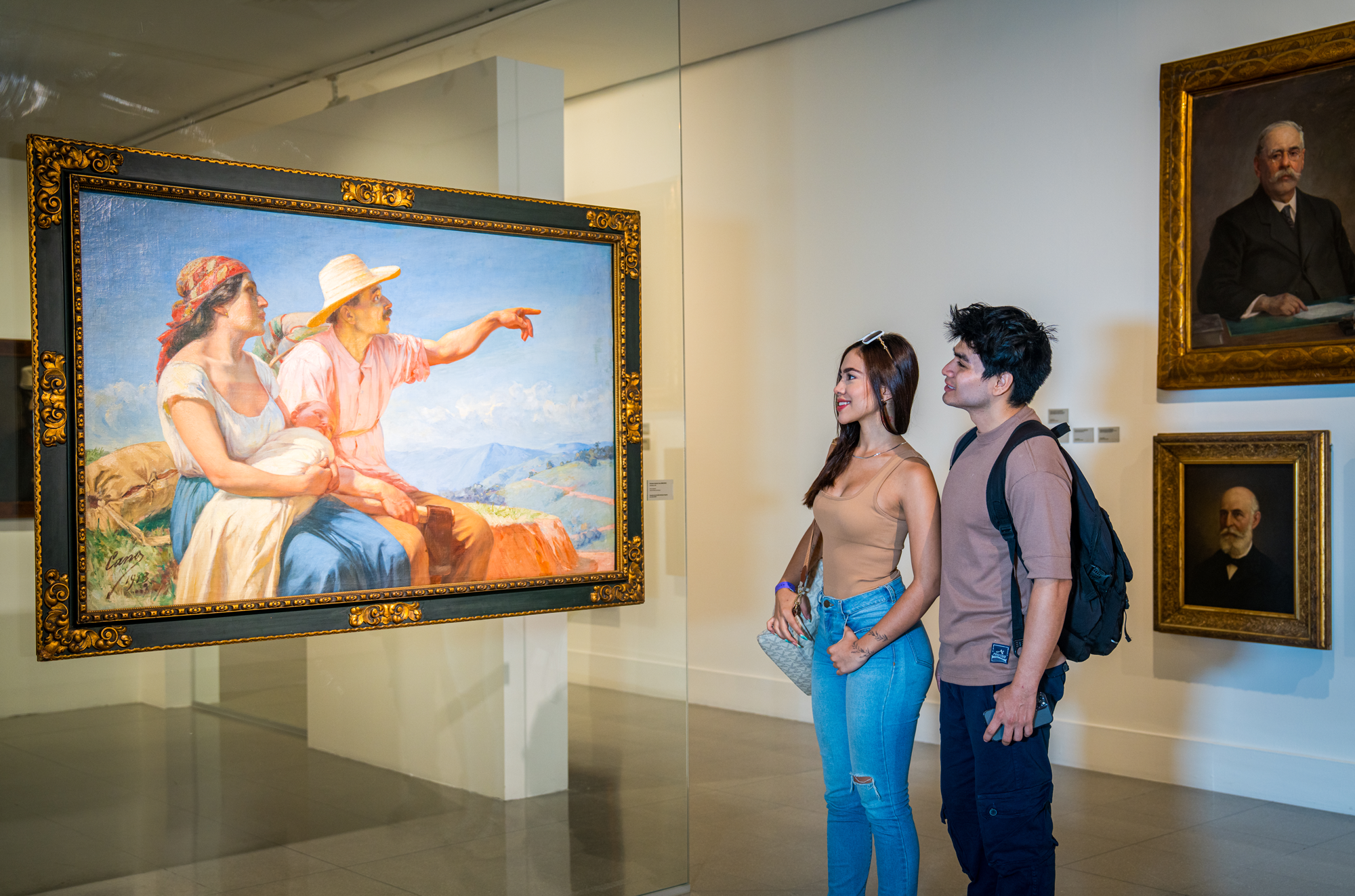 Dos personas observando una pintura en un museo, con otras pinturas en la pared.