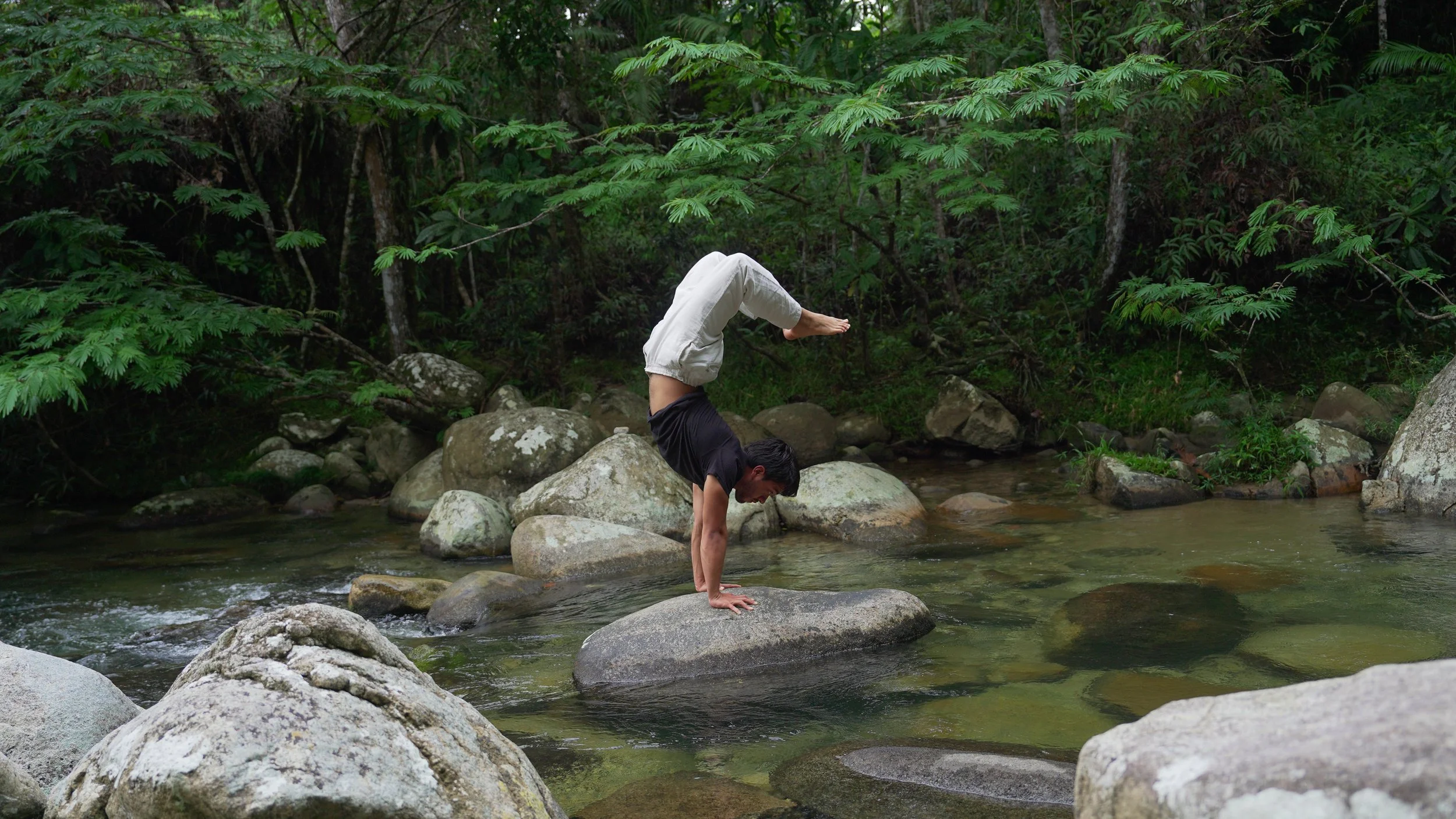 Hombre haciendo equilibrio en manos sobre una roca en un río rodeado de vegetación