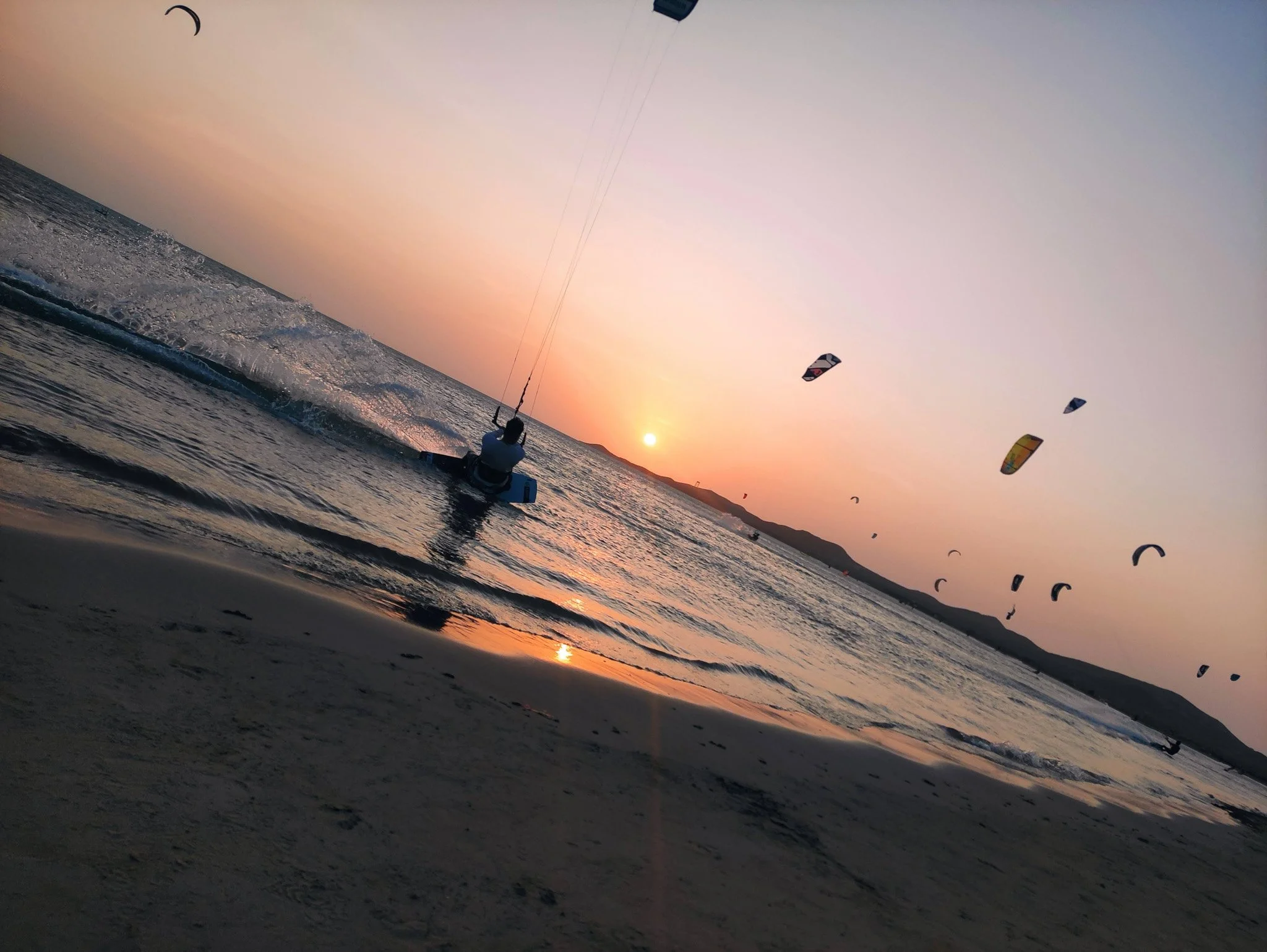 Atardecer en la playa con personas kite surf en el agua y un cielo colorido