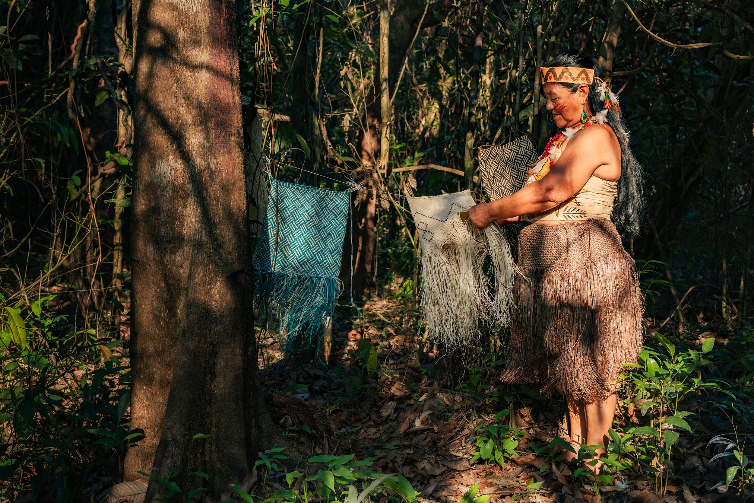 Una mujer indígena en un bosque tropical, con accesorios tradicionales, sosteniendo telas o fibras Naturales.