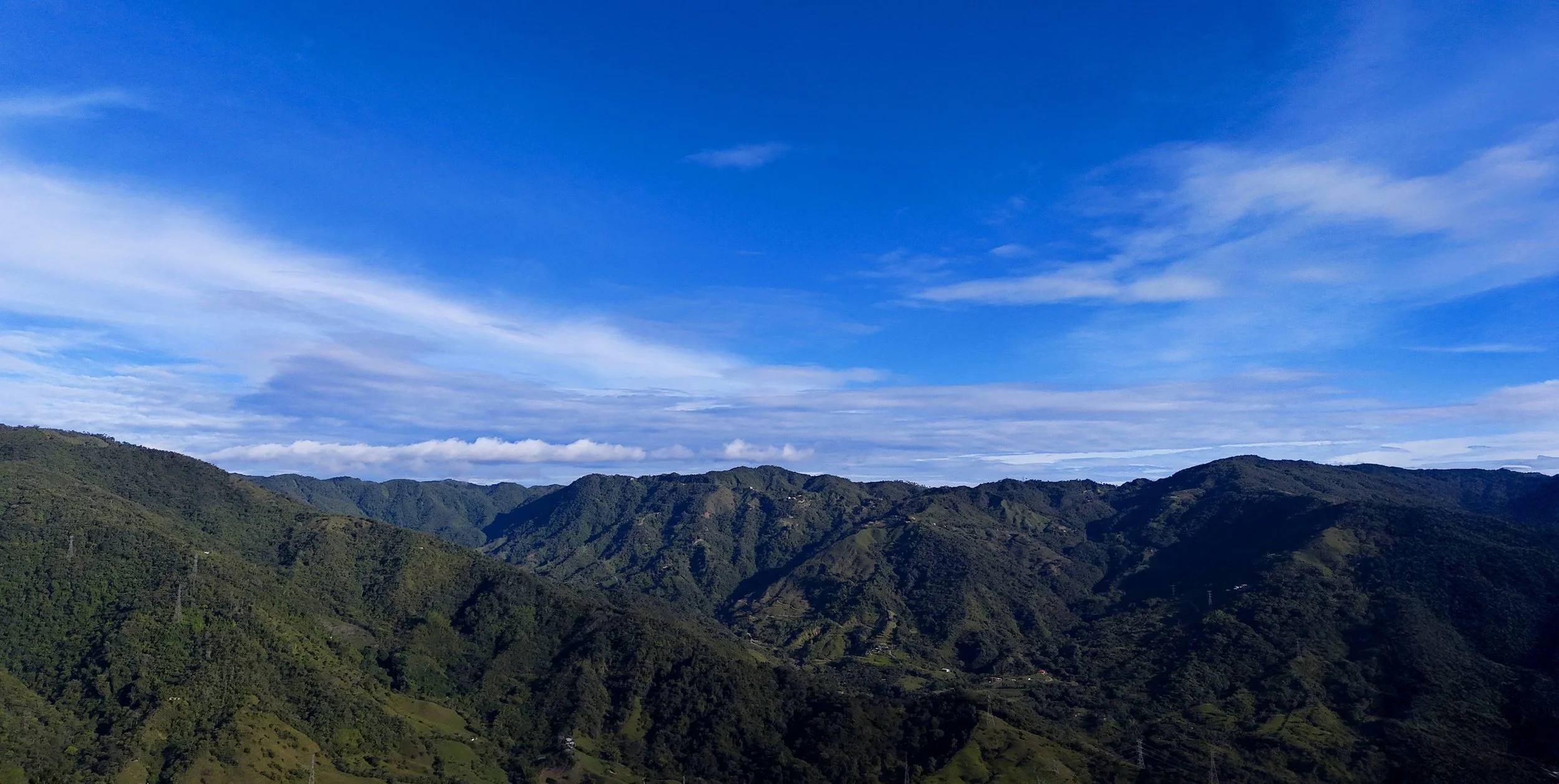 Montañas verdes con cielo azul y nubes delgadas.