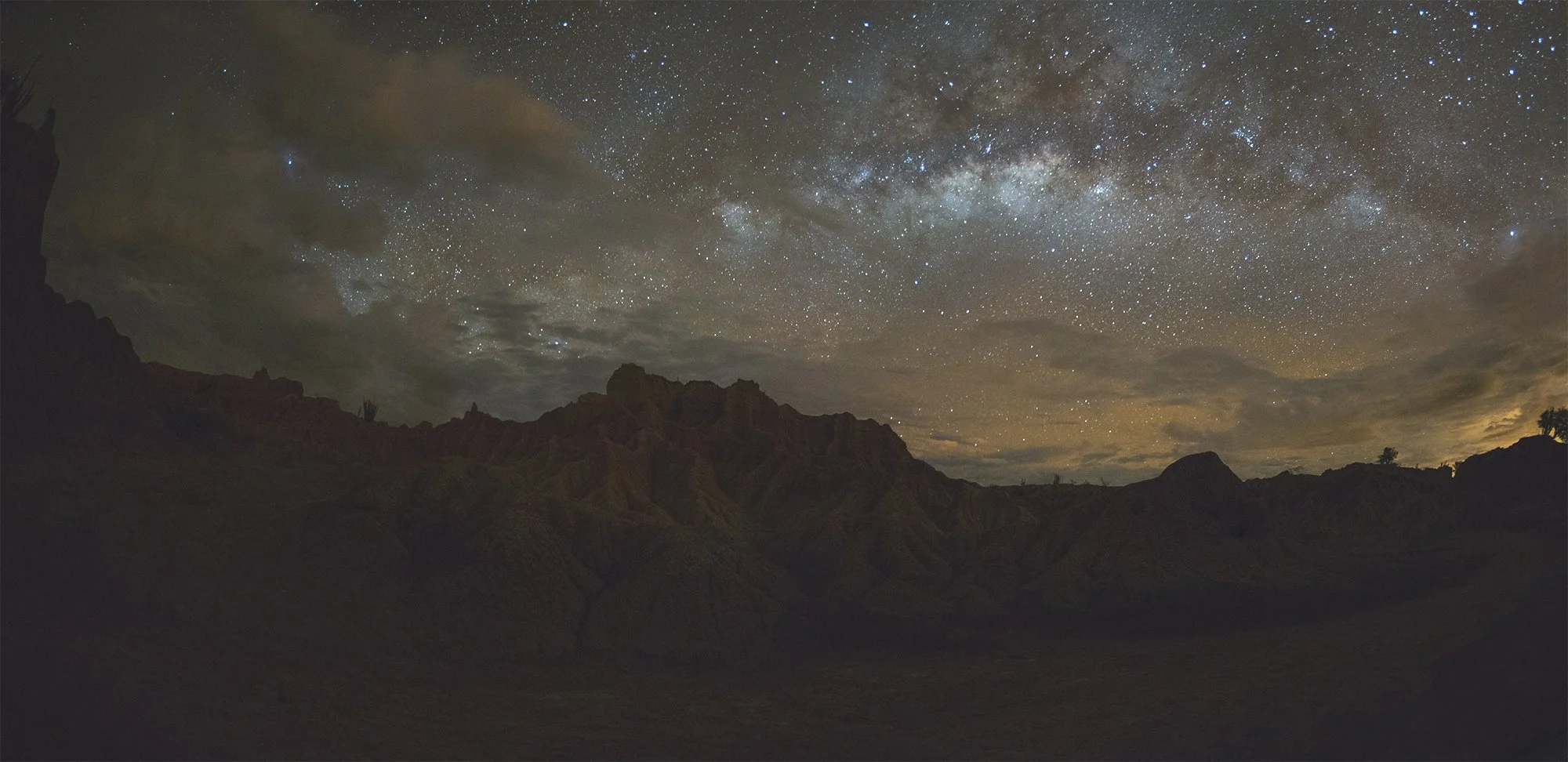 Cielo estrellado y la Vía Láctea sobre una cordillera montañosa en la noche.