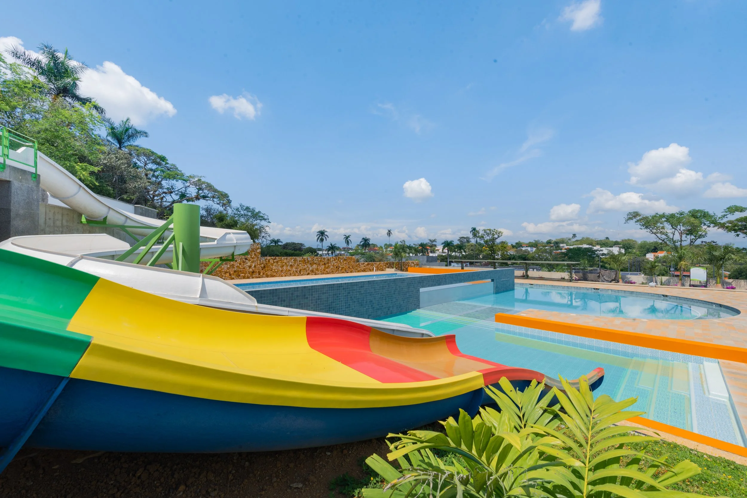 Piscina con toboganes de agua de colores brillantes en un parque acuático, con vegetación y cielo despejado en el fondo.