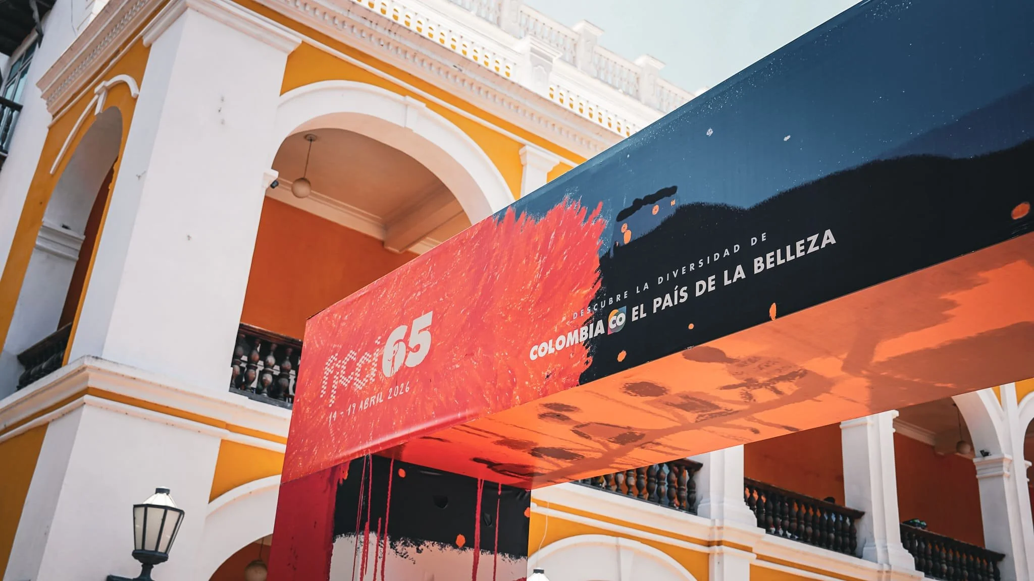 Edificio con color amarillo y blanco, cartel promocional sobre evento cultural en Colombia durante del 14 al 19 de abril de 2026.