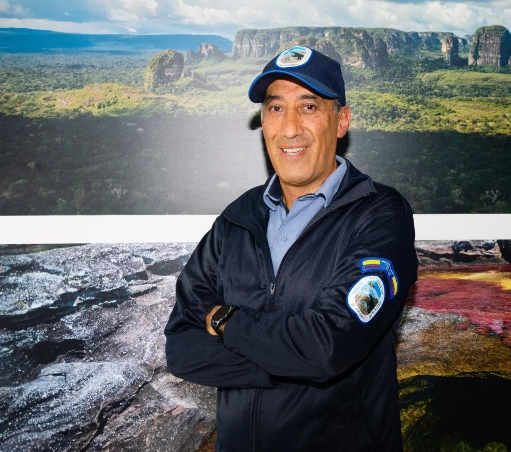 Hombre con chaqueta y gorra de paracaidismo en un fondo de paisaje natural, montañas y selva.