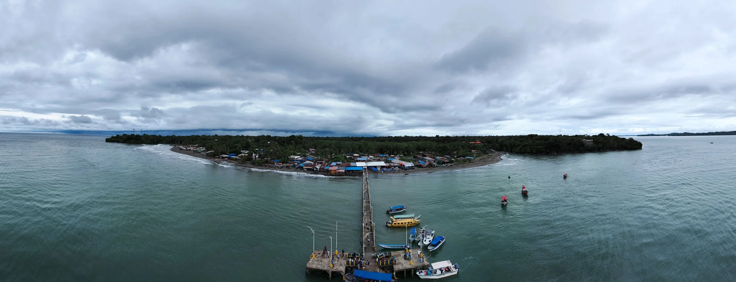 Vista aérea de una isla con un muelle y barcos amarrados en el mar, debajo de un cielo nublado.