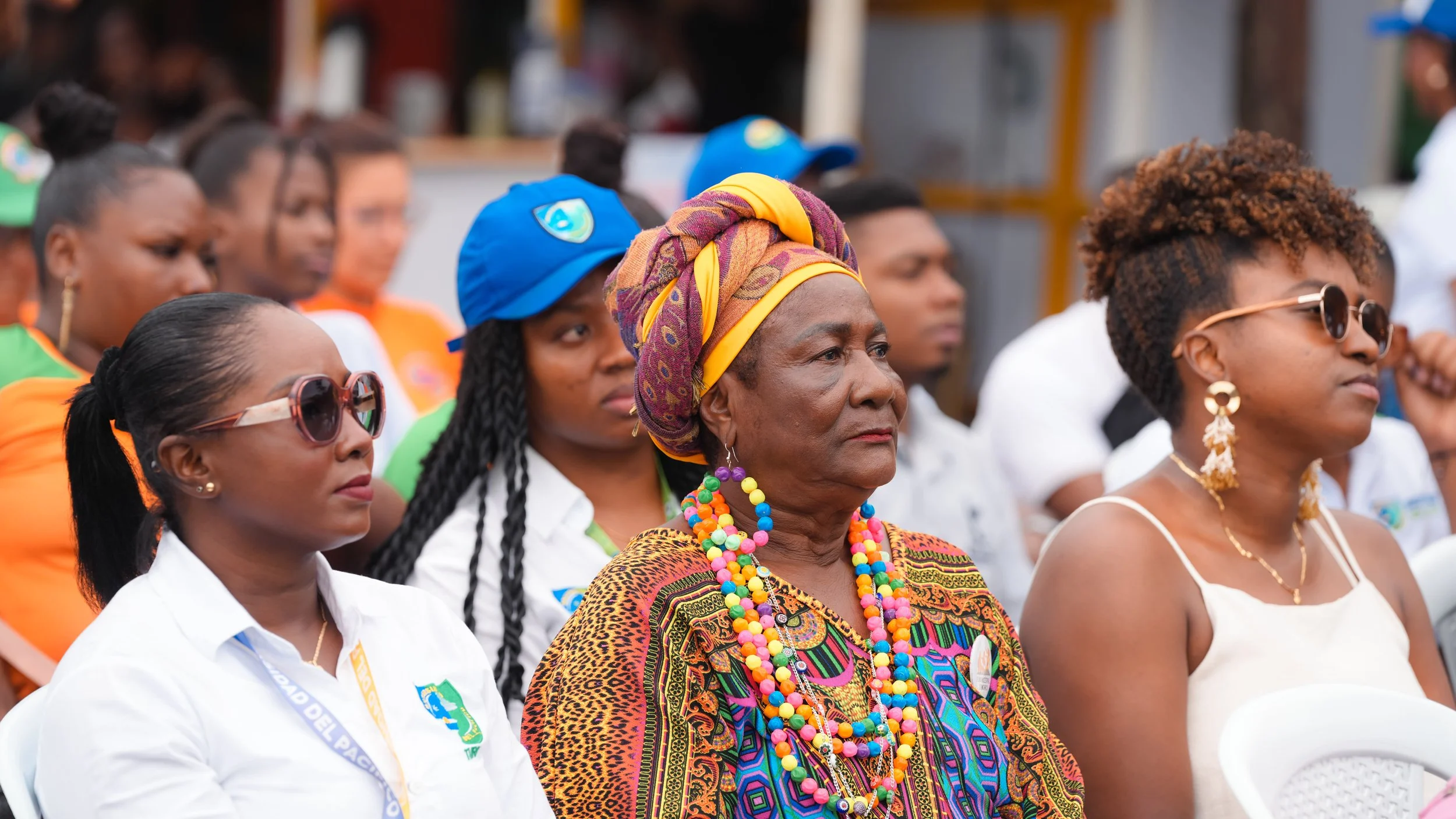 Grupo de mujeres en un evento al aire libre con ropa colorida y accesorios, algunas usando gafas en un ambiente festivo o cultural.