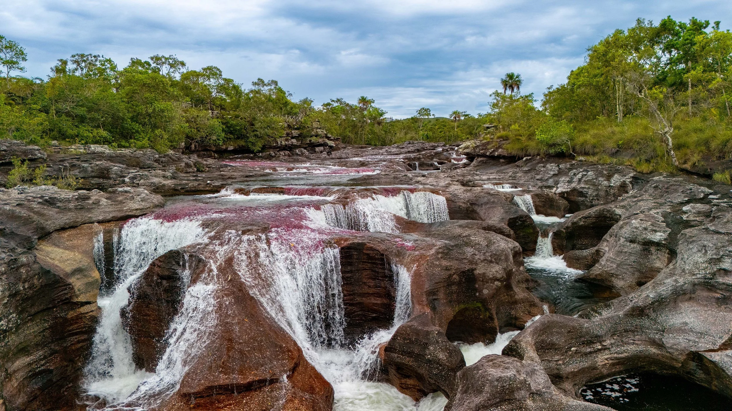 Cascada en medio de un entorno natural con árboles verdes y cielo nublado