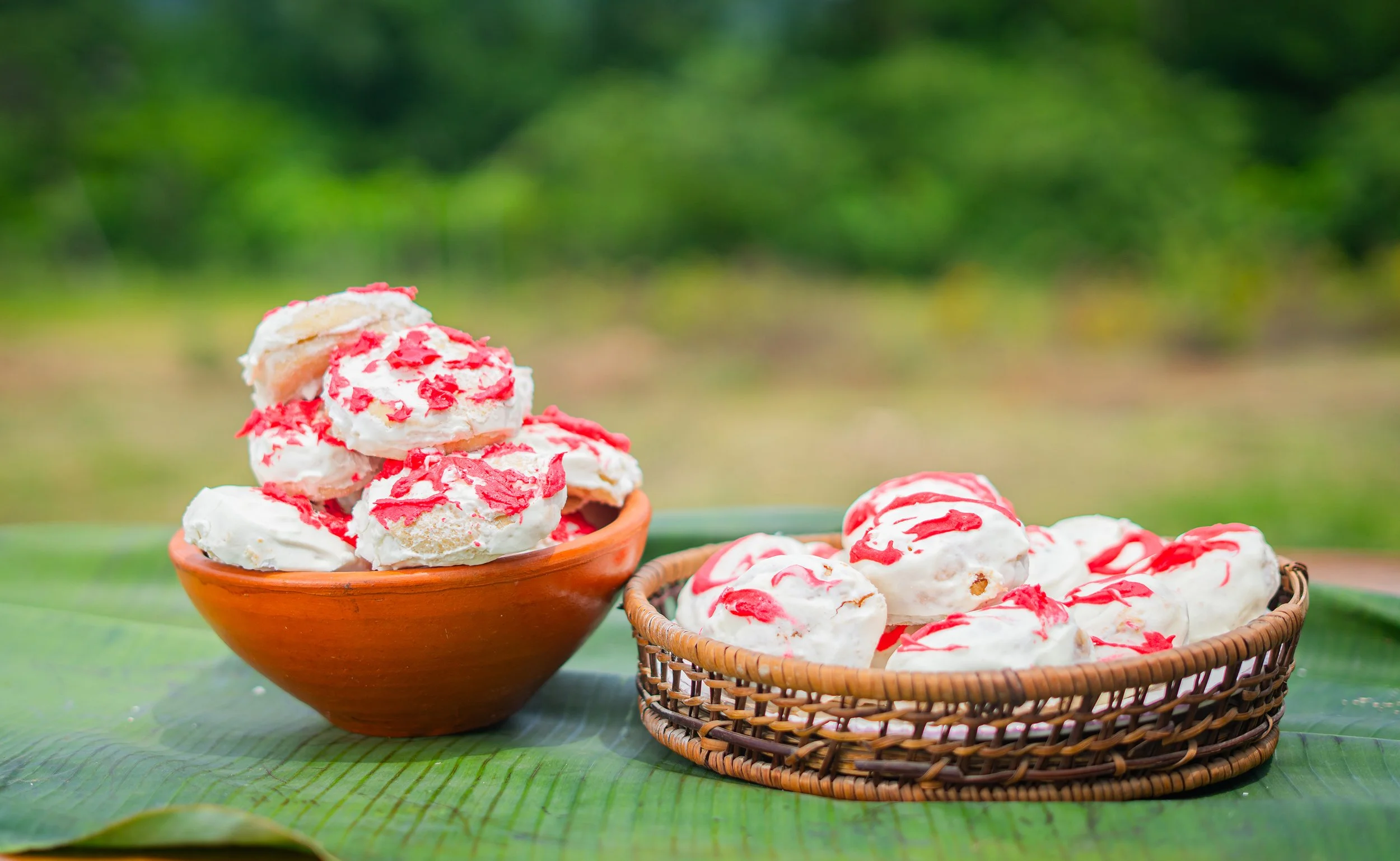 Tazones con helados de vainilla y jarabe de fresa, uno en una bandeja de mimbre y otro en un cuenco de cerámica, en un entorno natural con fondo de árboles verdes.