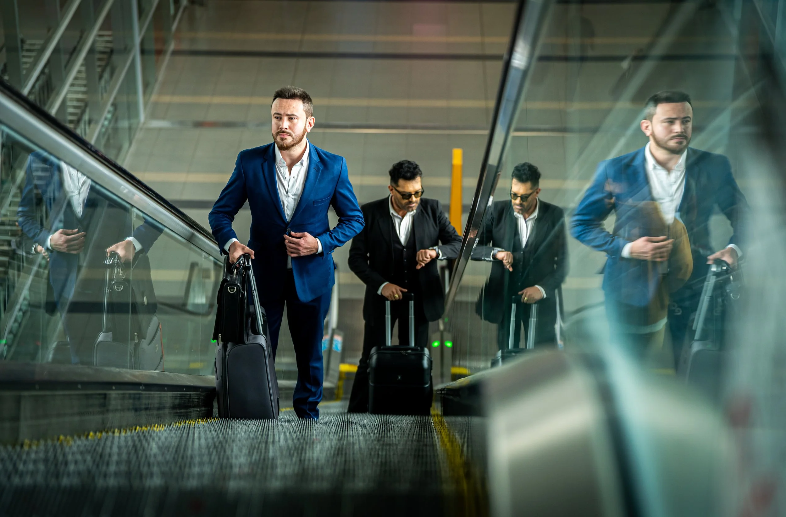 Hombres de negocios con maletines y vestimenta formal en una escalera mecánica en un aeropuerto.