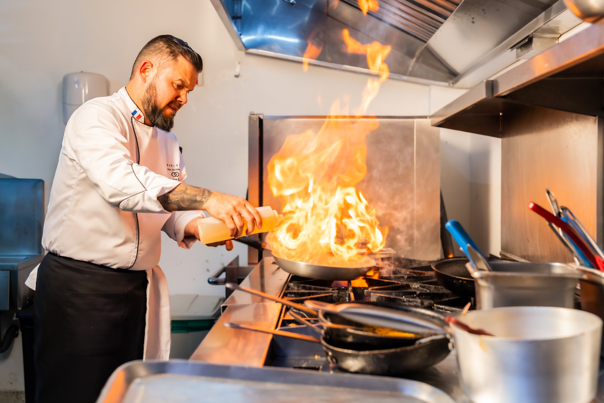 Chef cocinando en una estufa con llamas ardientes en una cocina profesional.