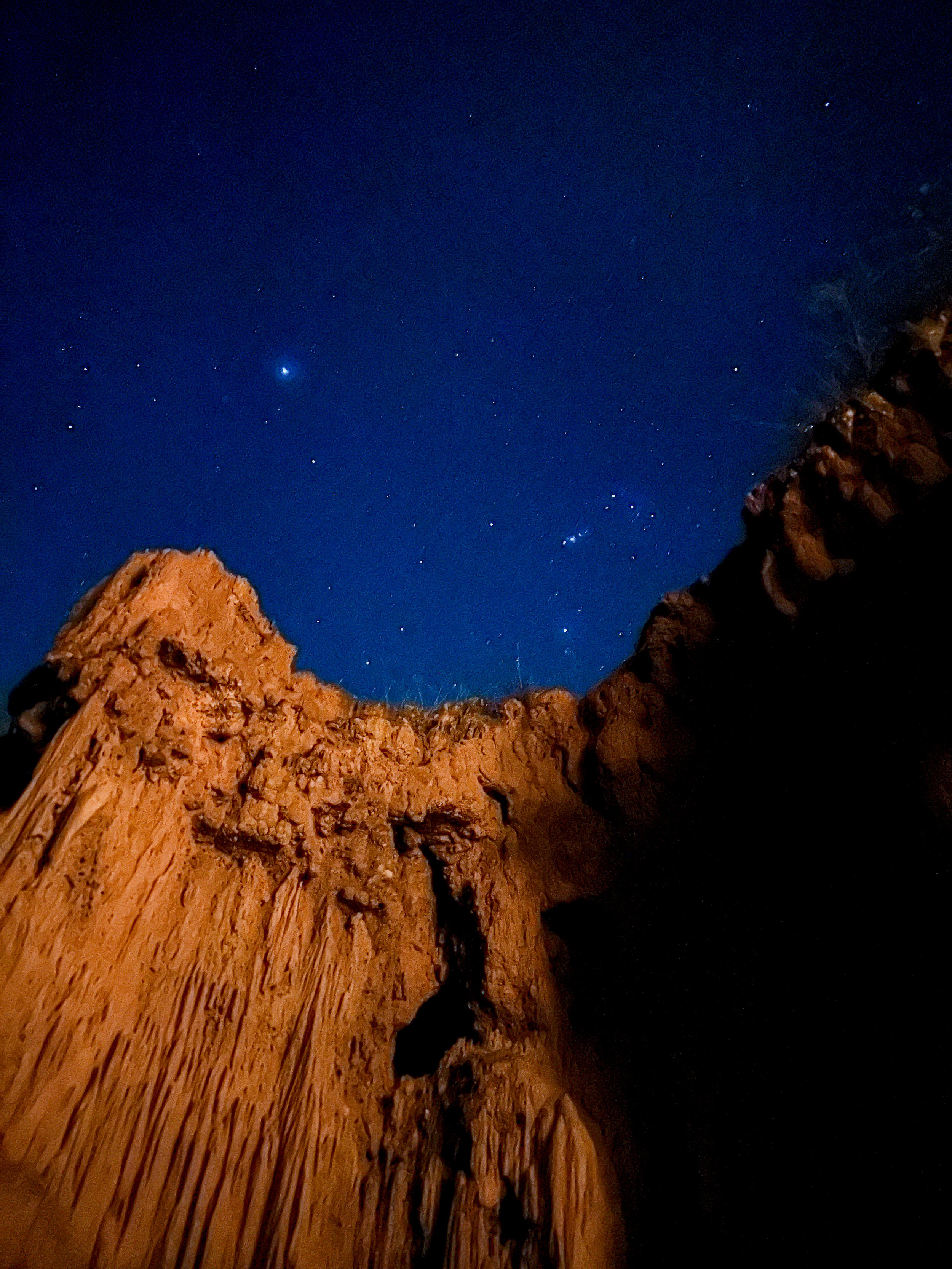 Vista de un cielo estrellado con formaciones rocosas en primer plano, posiblemente en un cañón o área montańosa.