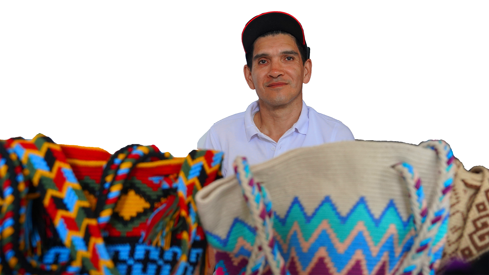 Hombre con gorra y camisa blanca, rodeado de tejidos tradicionales mexicanos con patrones coloridos y geométricos.