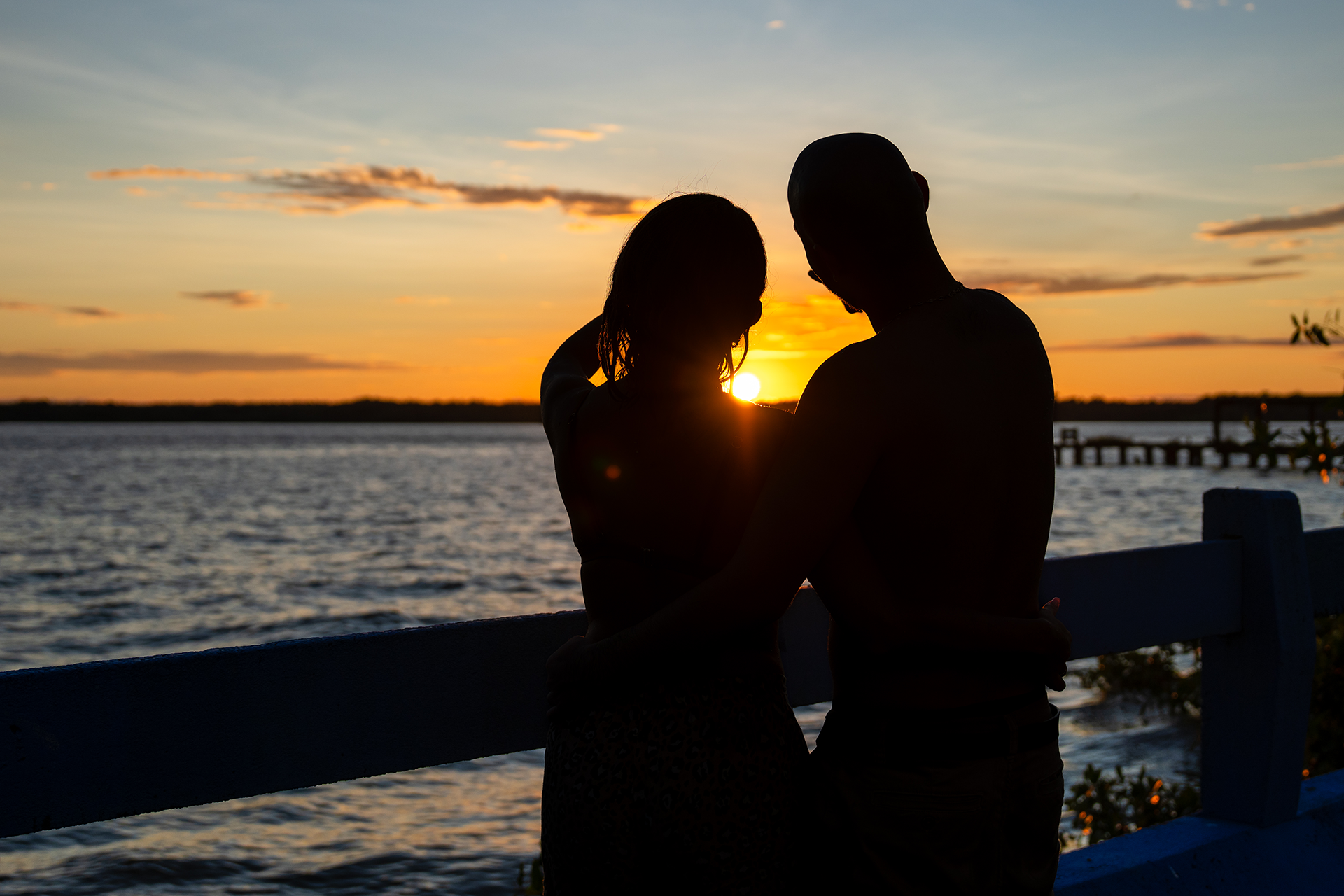 Pareja en silueta compartiendo un momento romántico durante la puesta del sol sobre un cuerpo de agua.