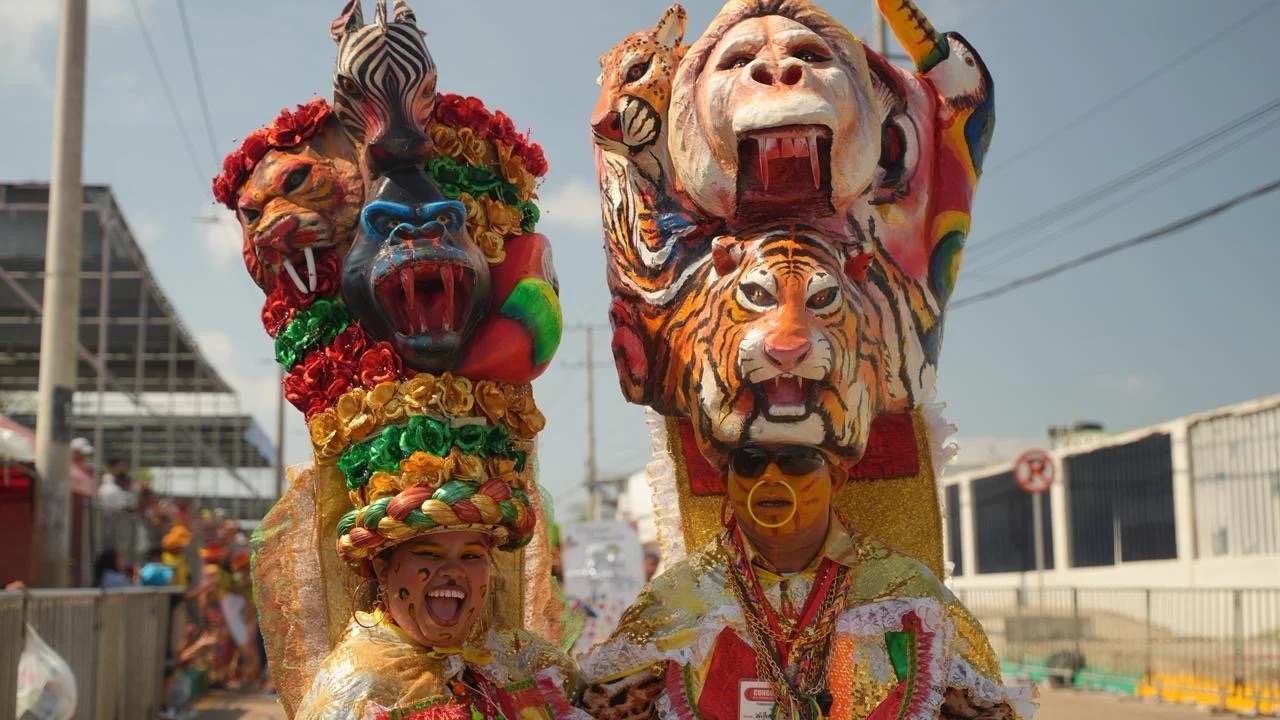 Dos personas con disfraces coloridos y máscaras de animales y criaturas míticas en un evento callejero.