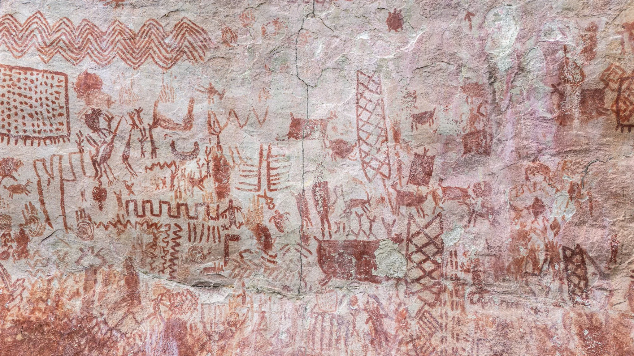 Pinturas rupestres en una pared de roca que muestran figuras humanas, animales y símbolos antiguos.