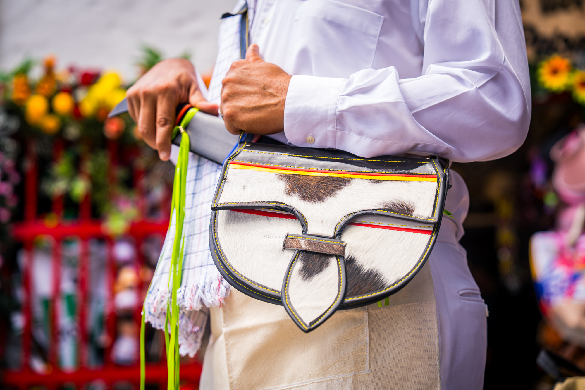Persona con camisa blanca sosteniendo una bolsa con patrón de caballo, en un entorno con flores y productos en el fondo.
