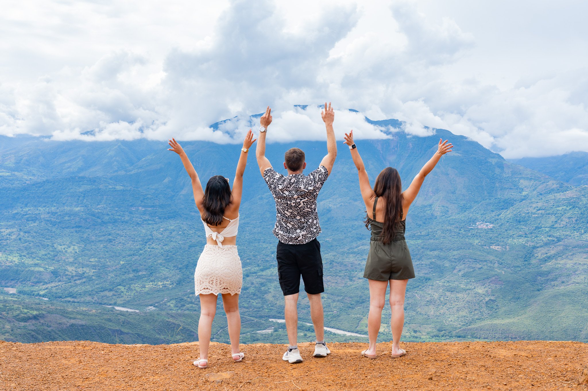 Cuatro personas de espaldas mirando una vista de montañas y nubes, con brazos levantados en señal de alegría o celebración.