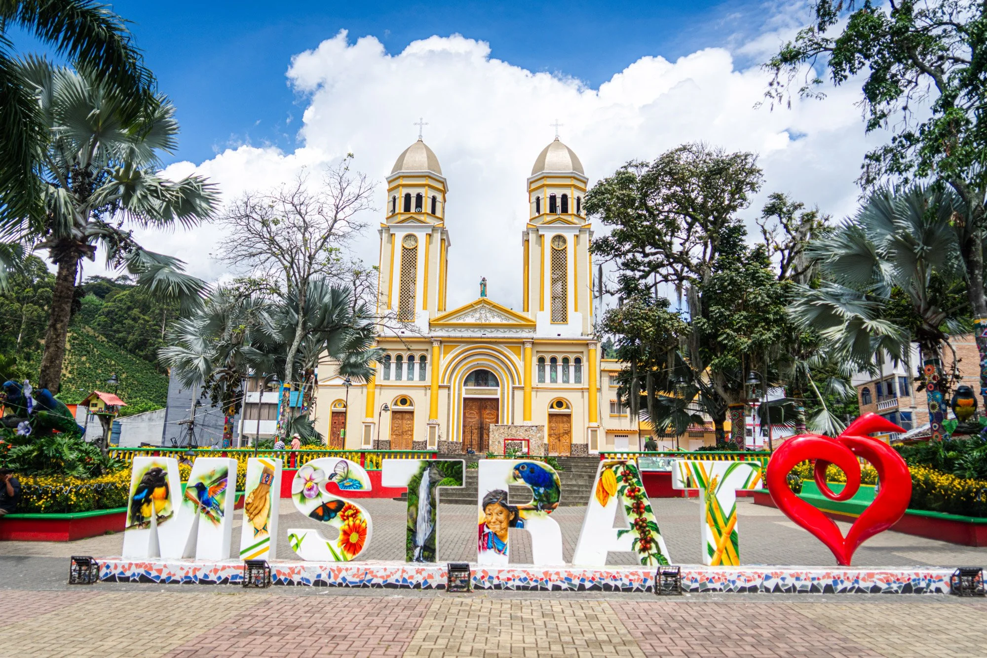 Fachada de una iglesia con dos torres en un día soleado y con árboles en el frente que enmarcan la estructura.