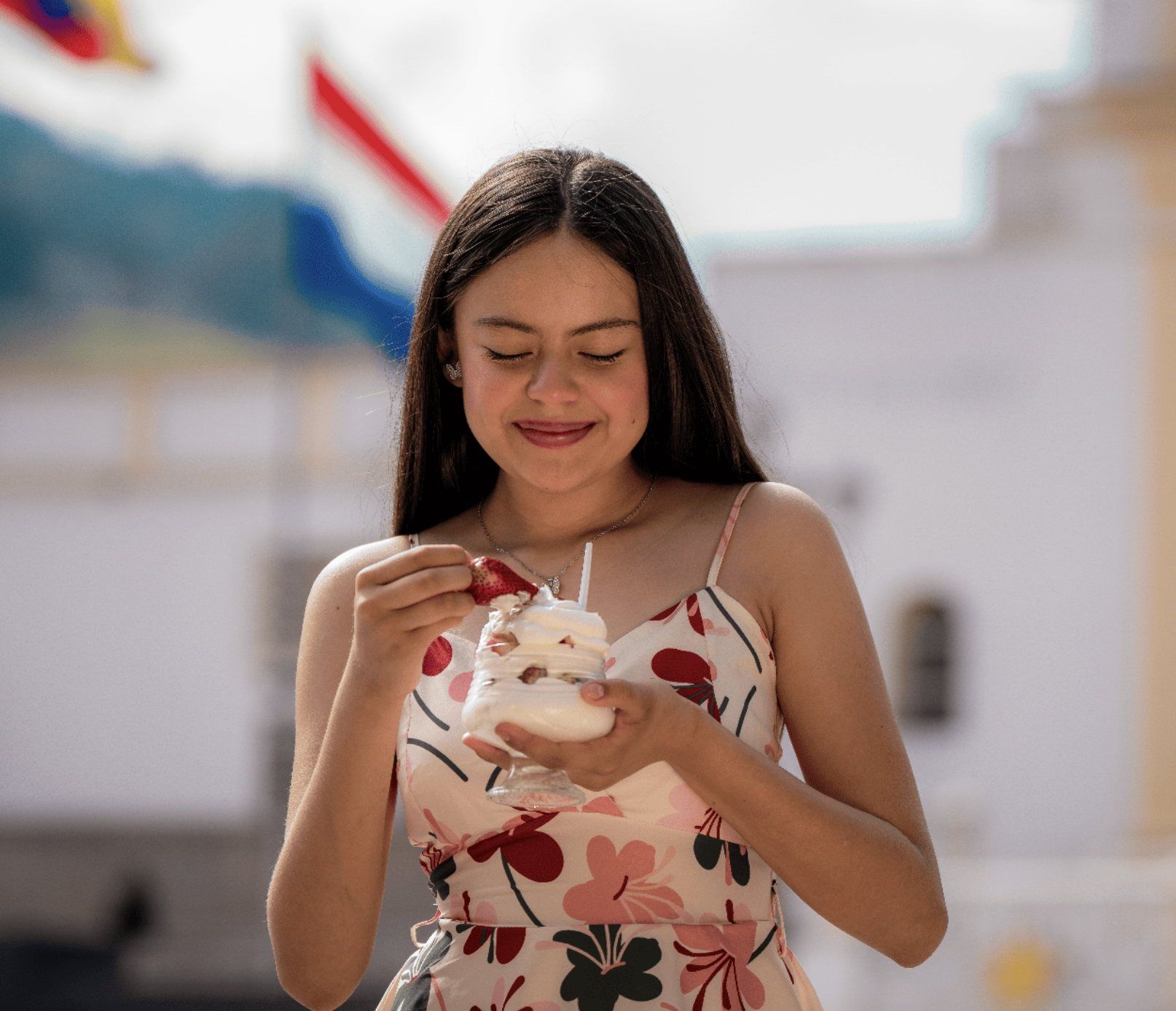 Joven sonriendo mientras mira un helado en un día soleado con globos de colores en el fondo.