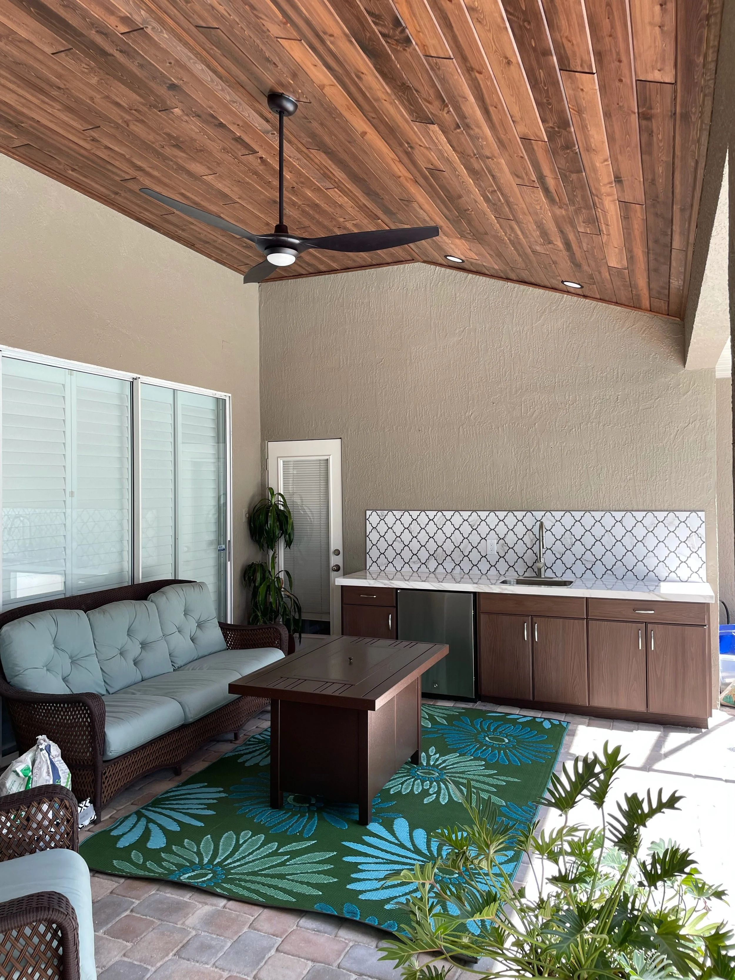 Outdoor lanai remodel in Windsor Place Belle Isle with wood-plank vaulted ceiling, outdoor kitchen with patterned tile backsplash, and seating area.
