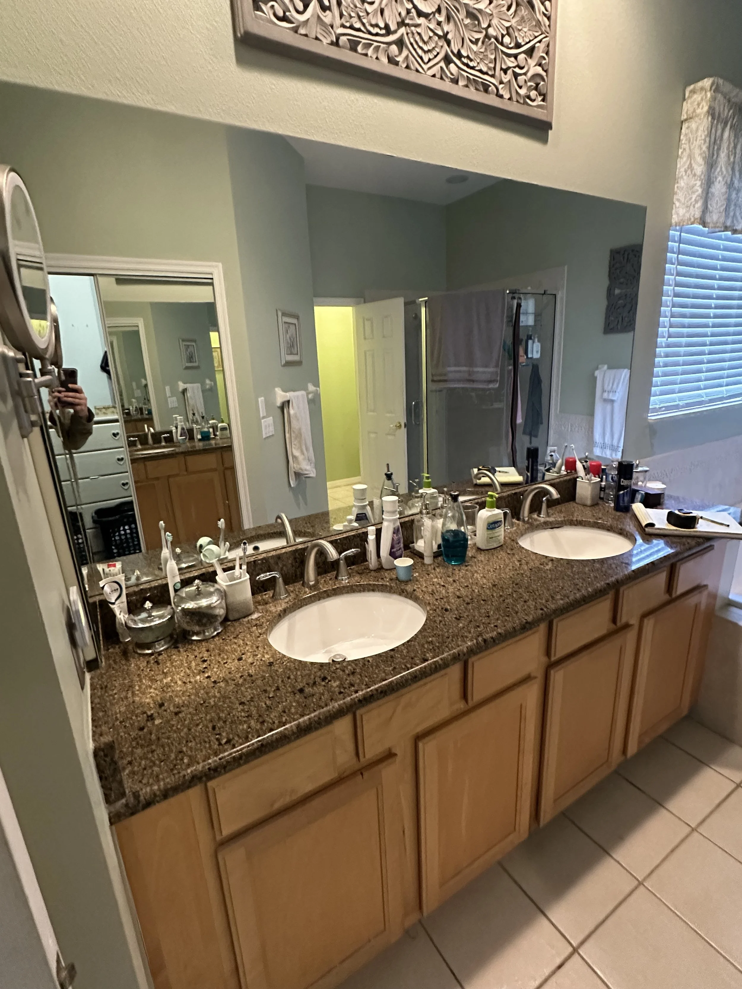 Dated double vanity with maple cabinets and brown granite countertops before the Heathrow primary bathroom remodel.