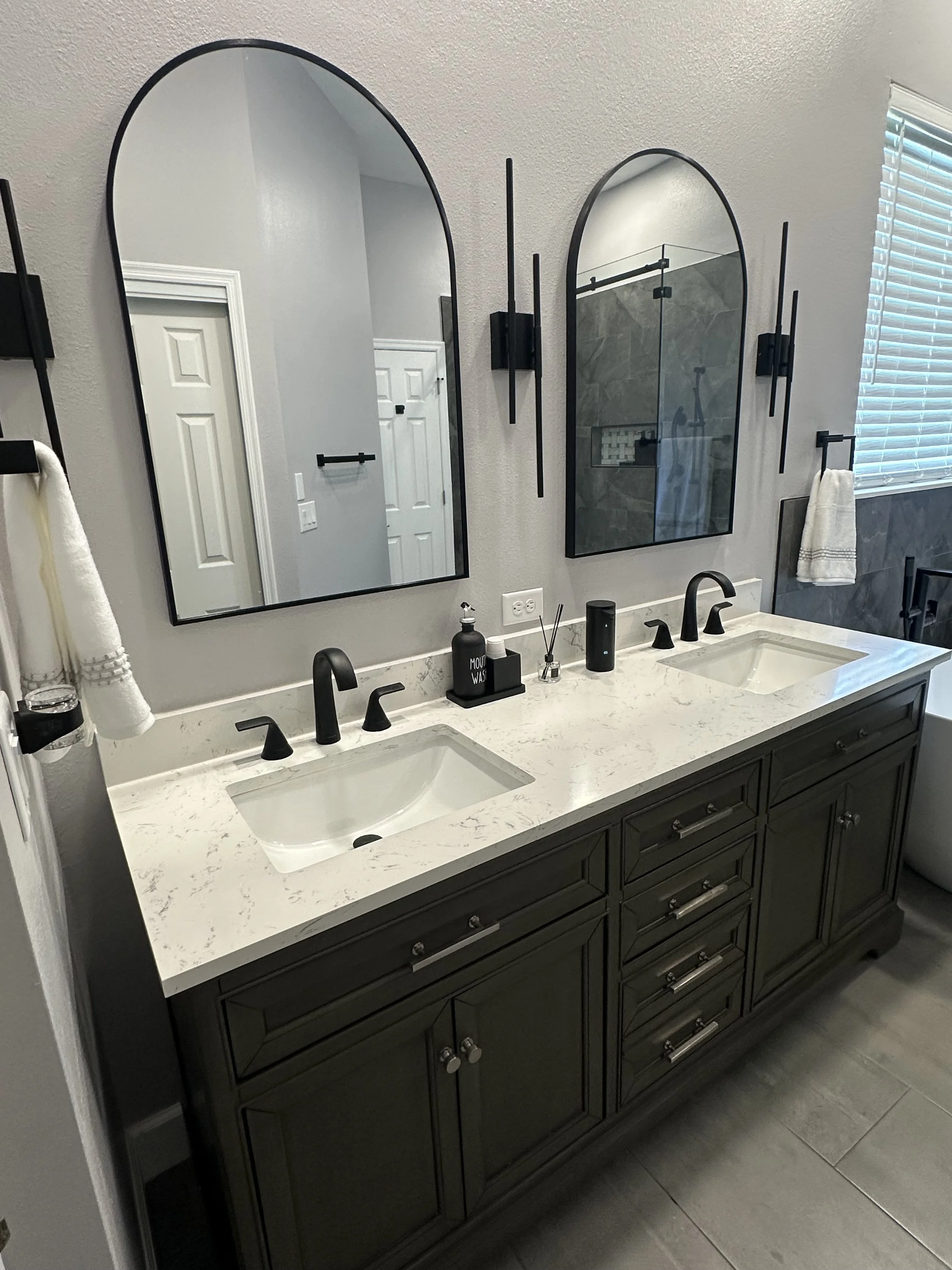 Primary bathroom remodel in Heathrow, Lake Mary with a charcoal double vanity, white quartz countertops, and arched black mirrors.
