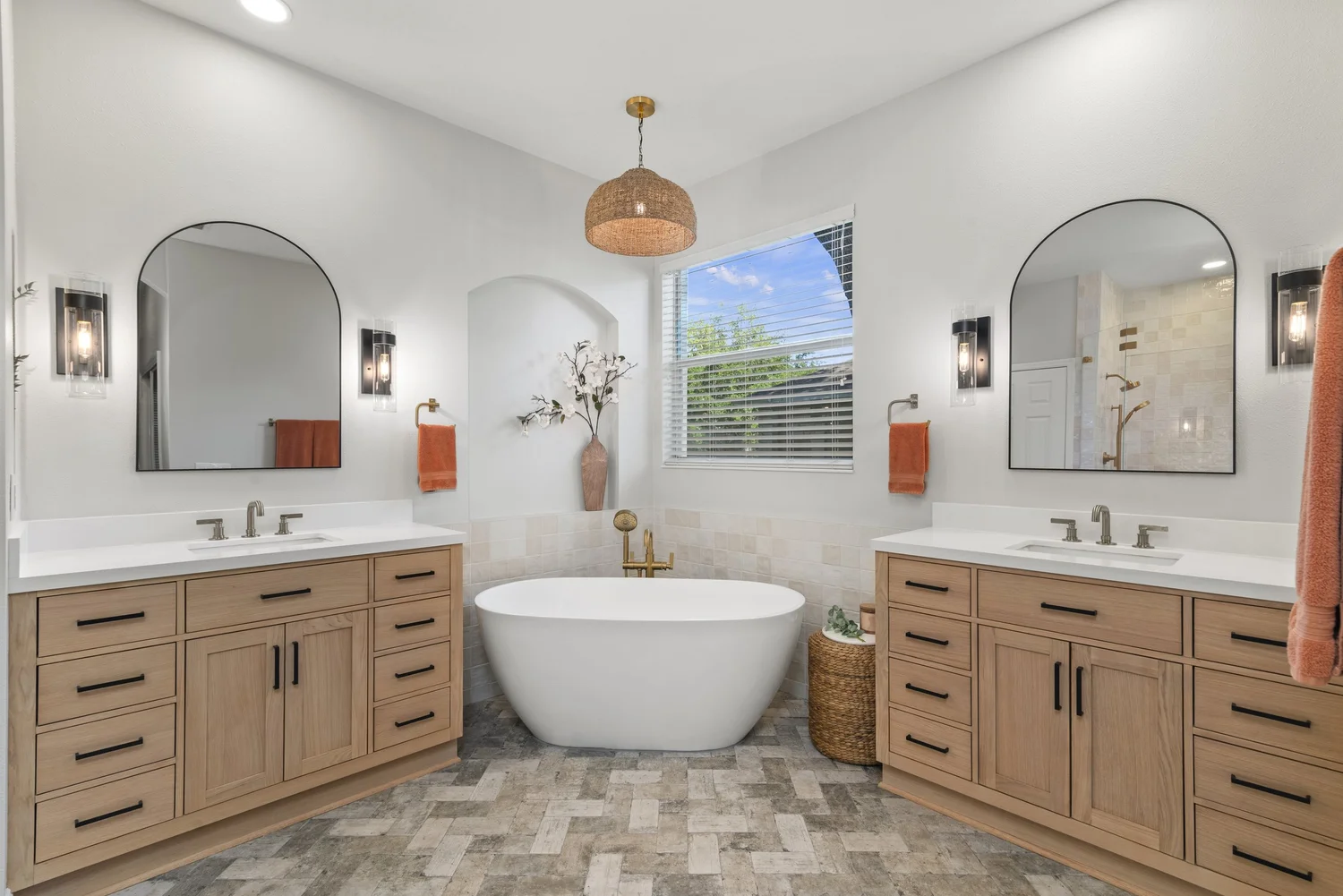 Bathroom remodel with a freestanding tub between two wood vanities and large mirrors