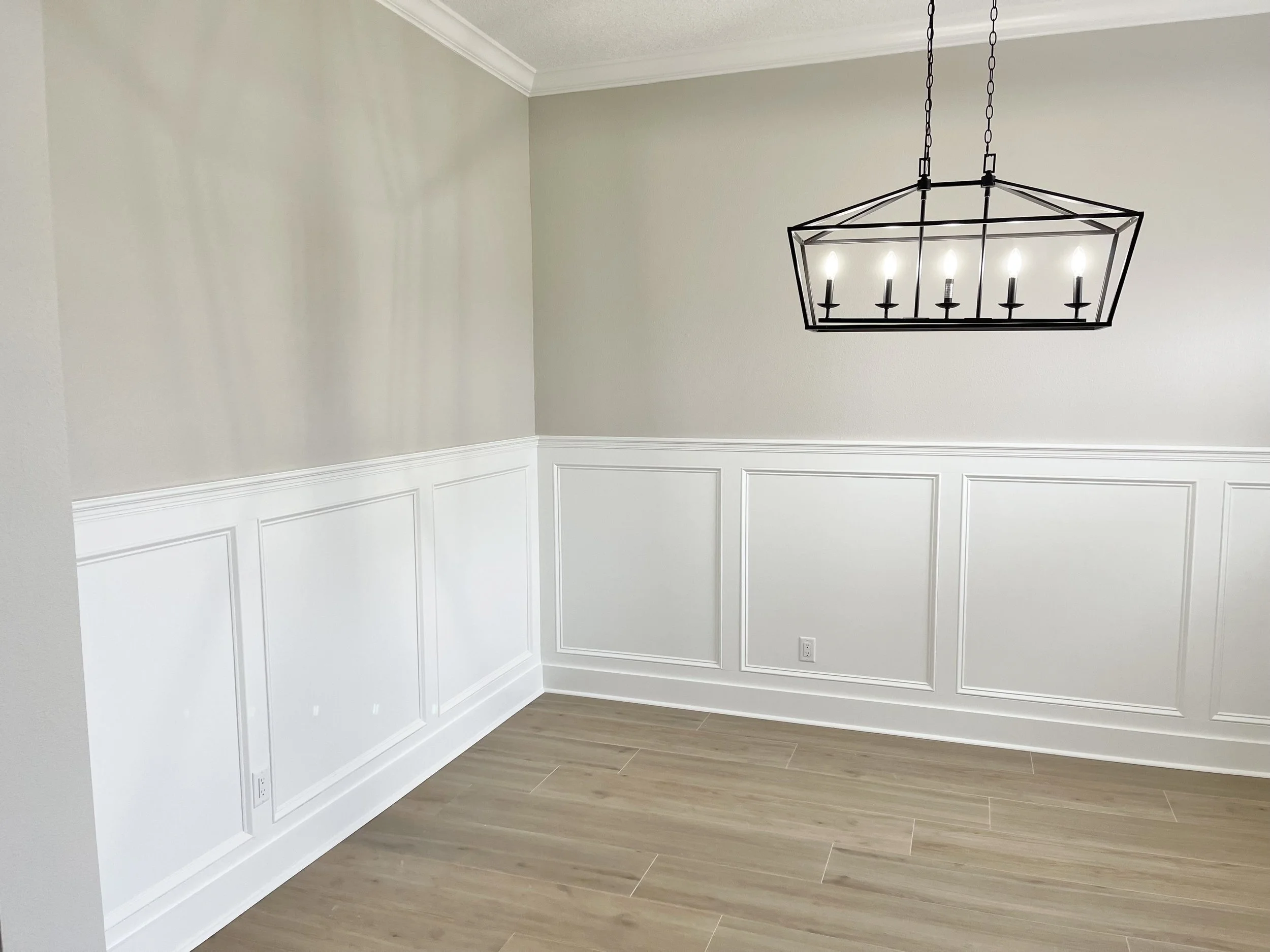 Modern dining room with geometric chandelier, wainscoting, and light wood flooring.