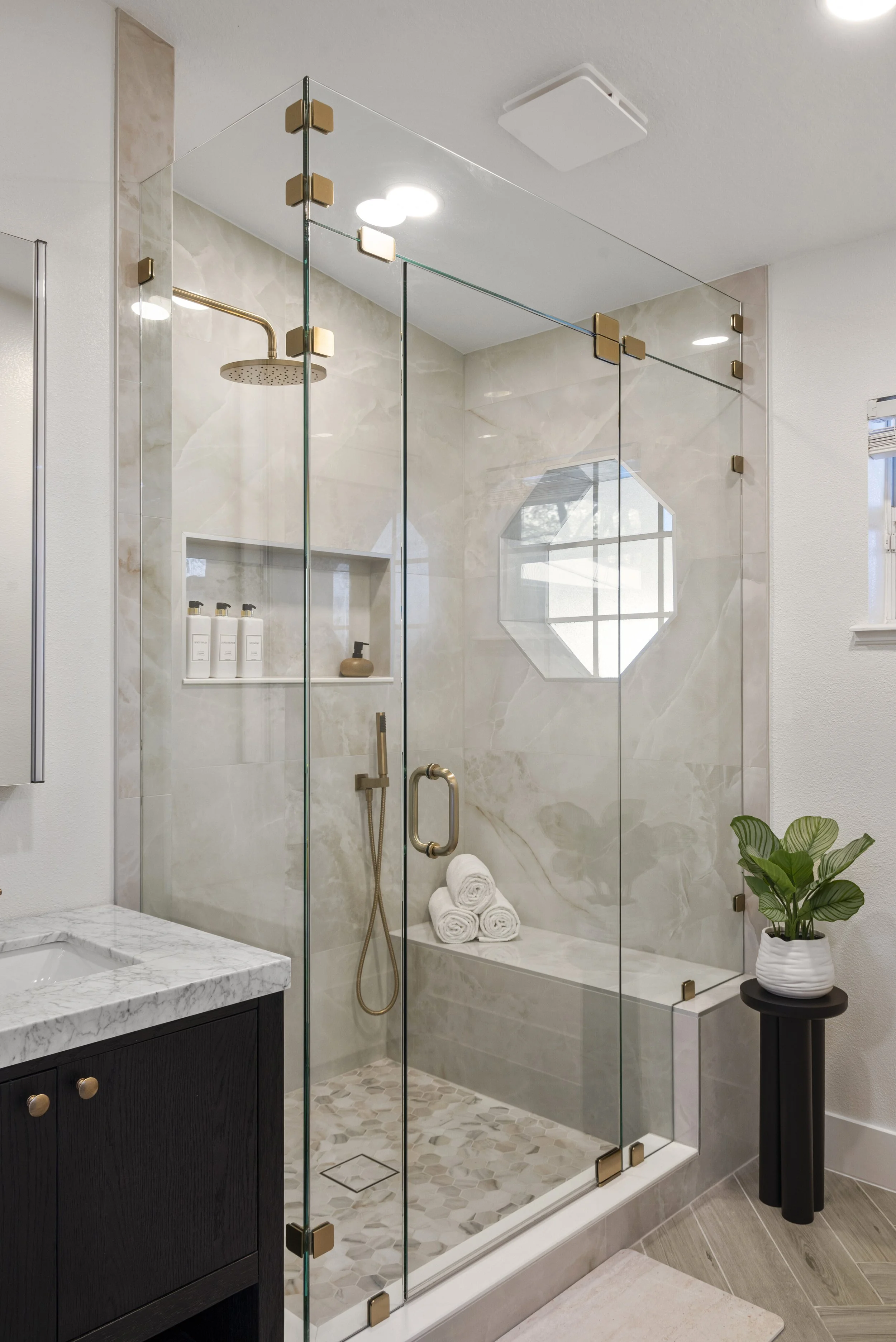 Primary bathroom remodel in Dunn Cove Apopka with walk-in shower, stone-look porcelain tile, brass fixtures, and octagonal window.