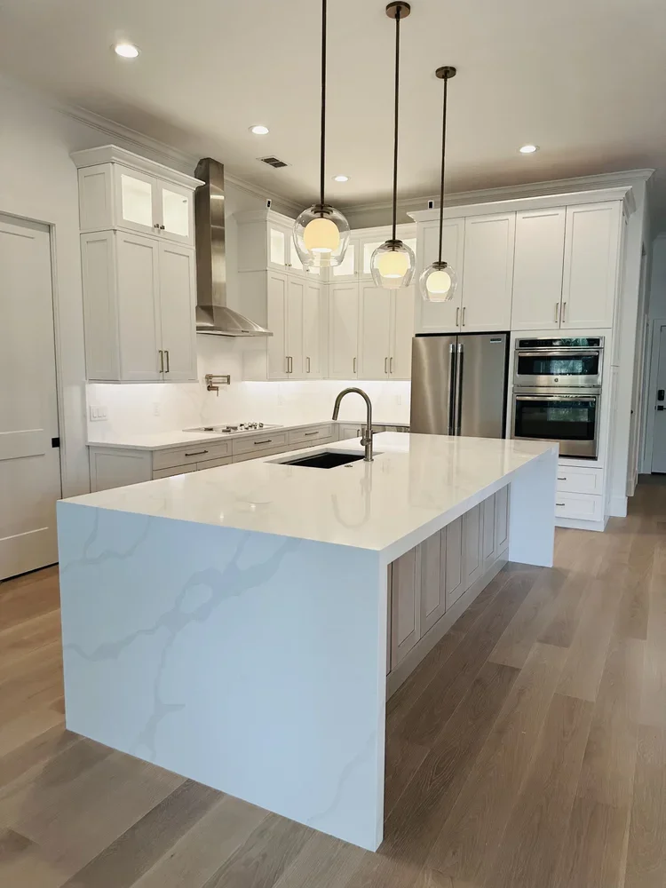 Modern kitchen with dark wood cabinets, white countertops, and a herringbone backsplash pattern. Features an island, stainless steel appliances, window with a view, and bar stools.