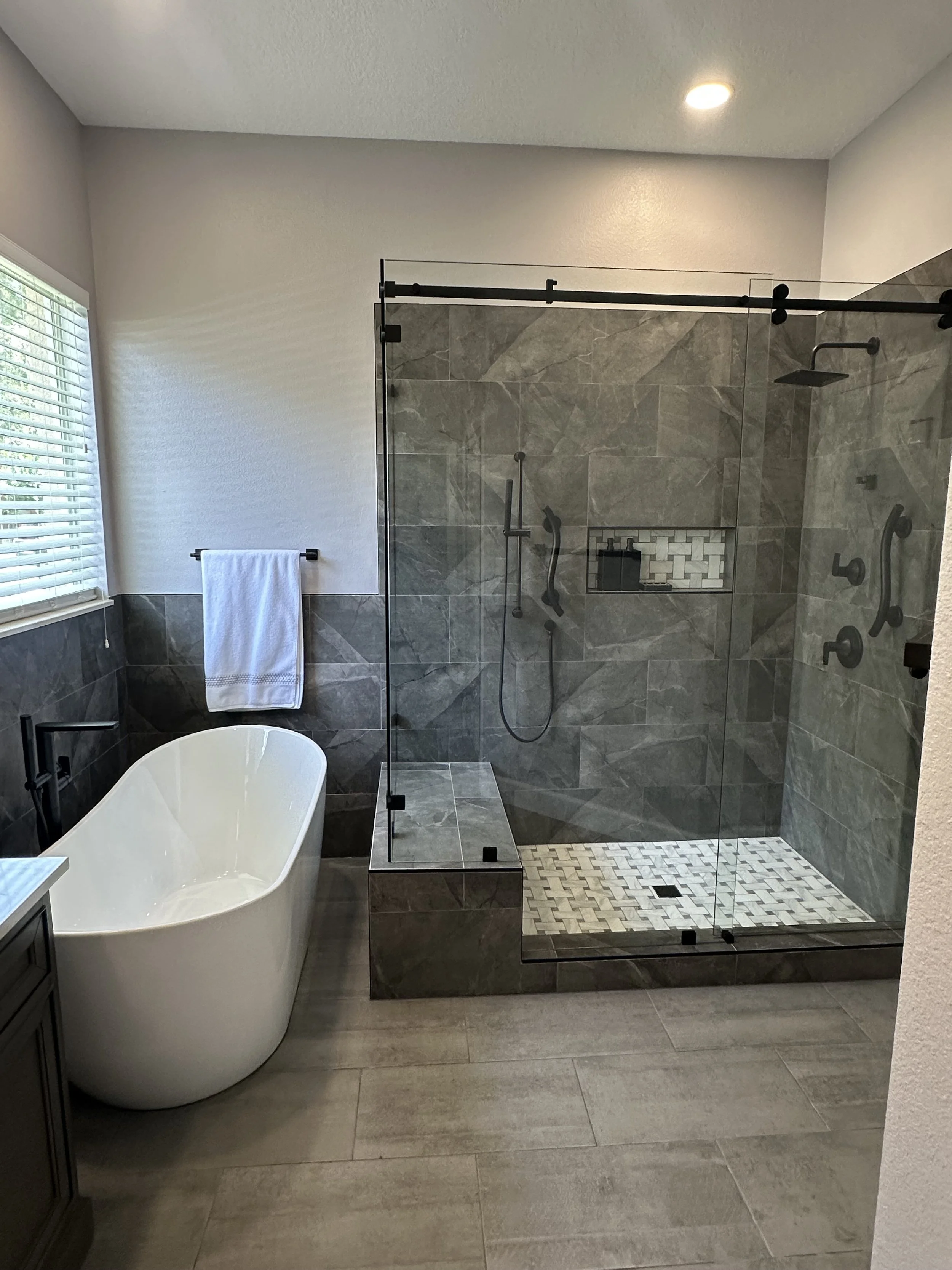 Lake Mary primary bathroom with a freestanding soaking tub and a glass walk-in shower finished in gray marble-look tile.