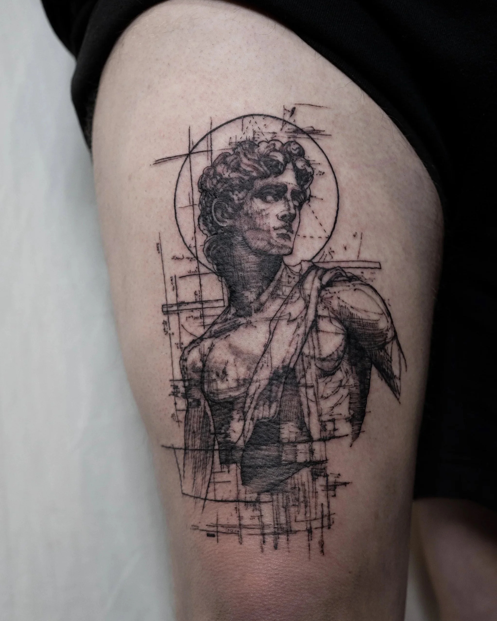 Jay c tattoo made a black ink tattoo of a classical sculpture style bust of a woman with short curly hair, with geometric and sketch-like lines around her, on a person's leg.