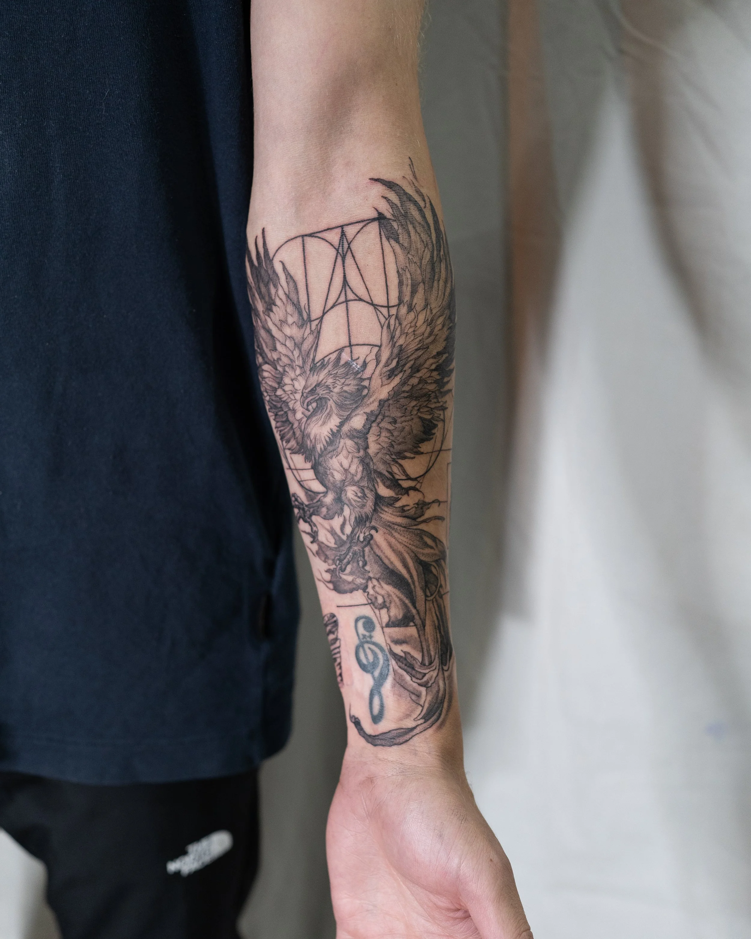 Tattoo artist in hove creates a phoenix with wings spread and a treble clef symbol on the forearm.