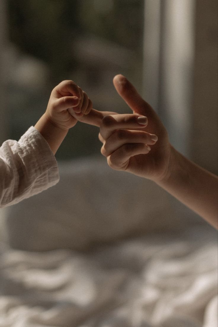 Mano de un bebé agarrando el dedo de un adulto con luz suave de fondo.