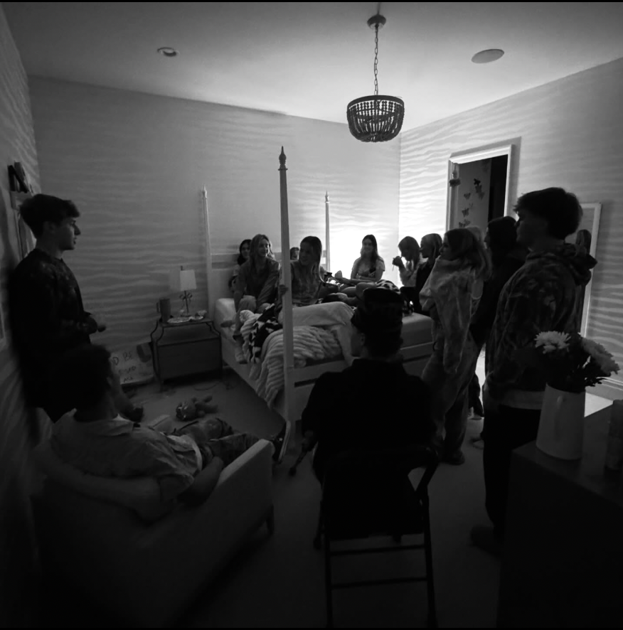 A black and white photo of a bunch of teenagers sitting together in a bedroom