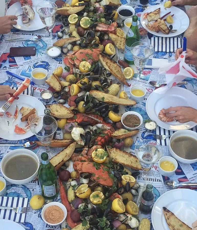 seafood spread on a table with hands getting food