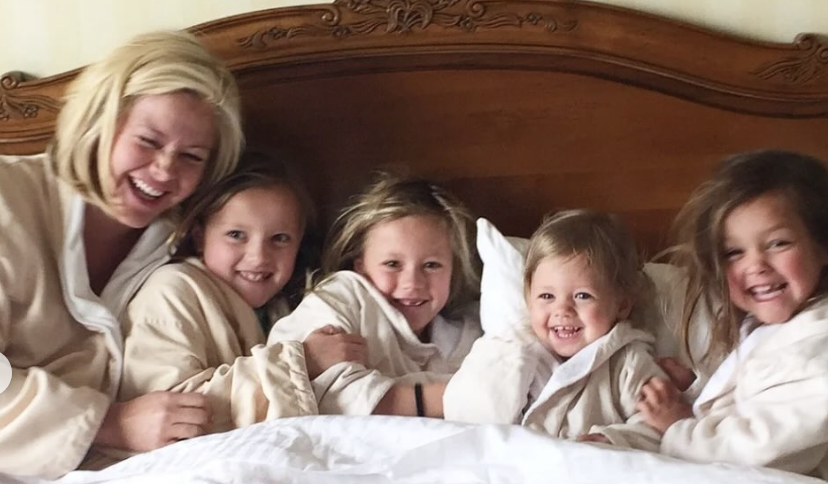 Kristin laughing with her four daughters in bed together