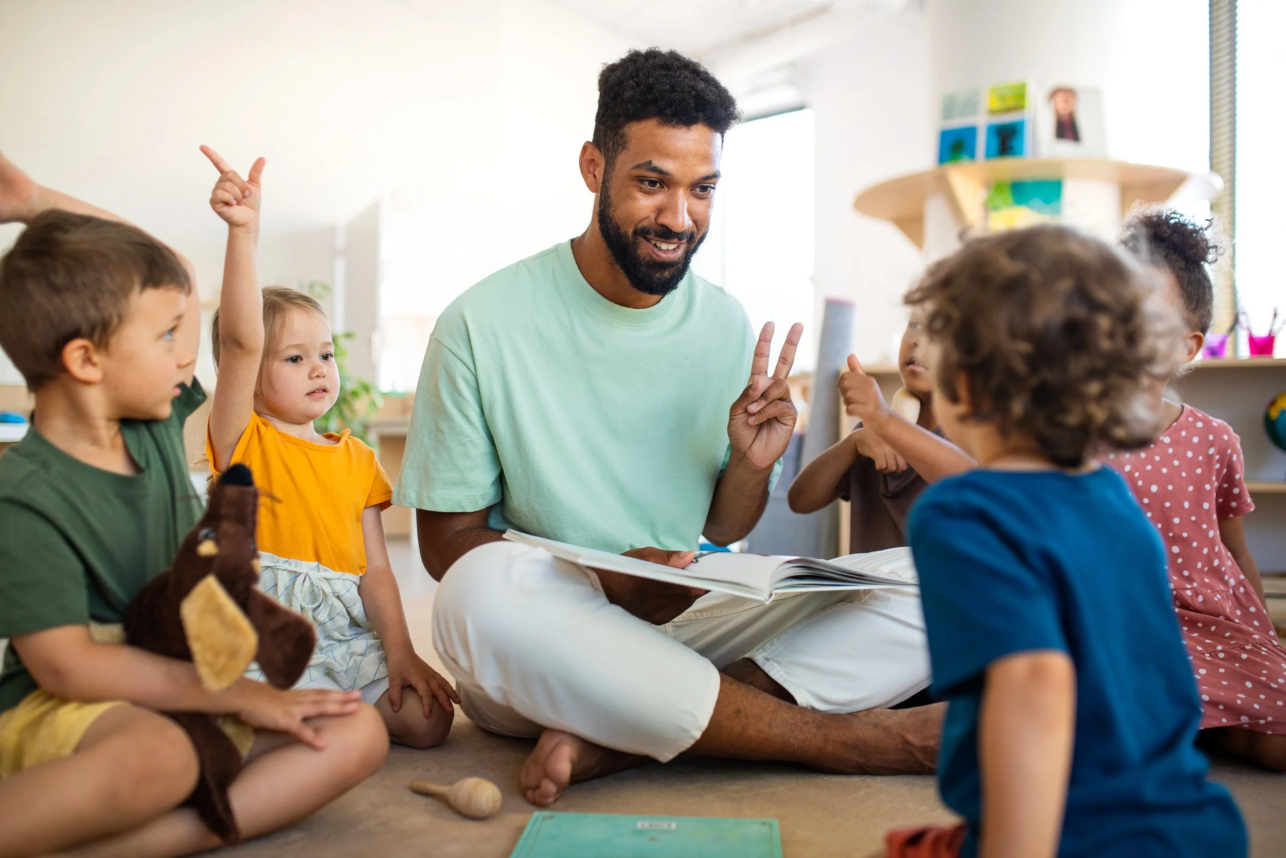 Teacher reading a story to a diverse group of children sitting on the floor in a classroom.