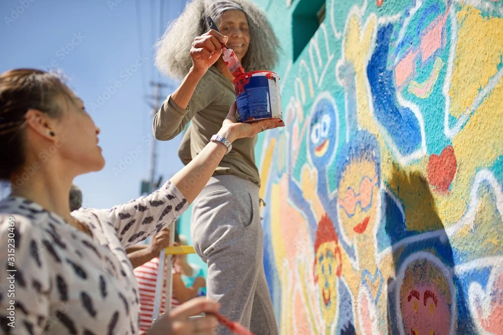 A woman and a girl painting a colorful mural on a wall outdoors.